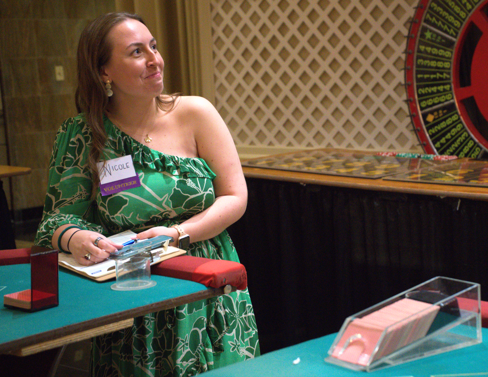 a woman in a green dress with a volunteer nametag smiling up to the side.