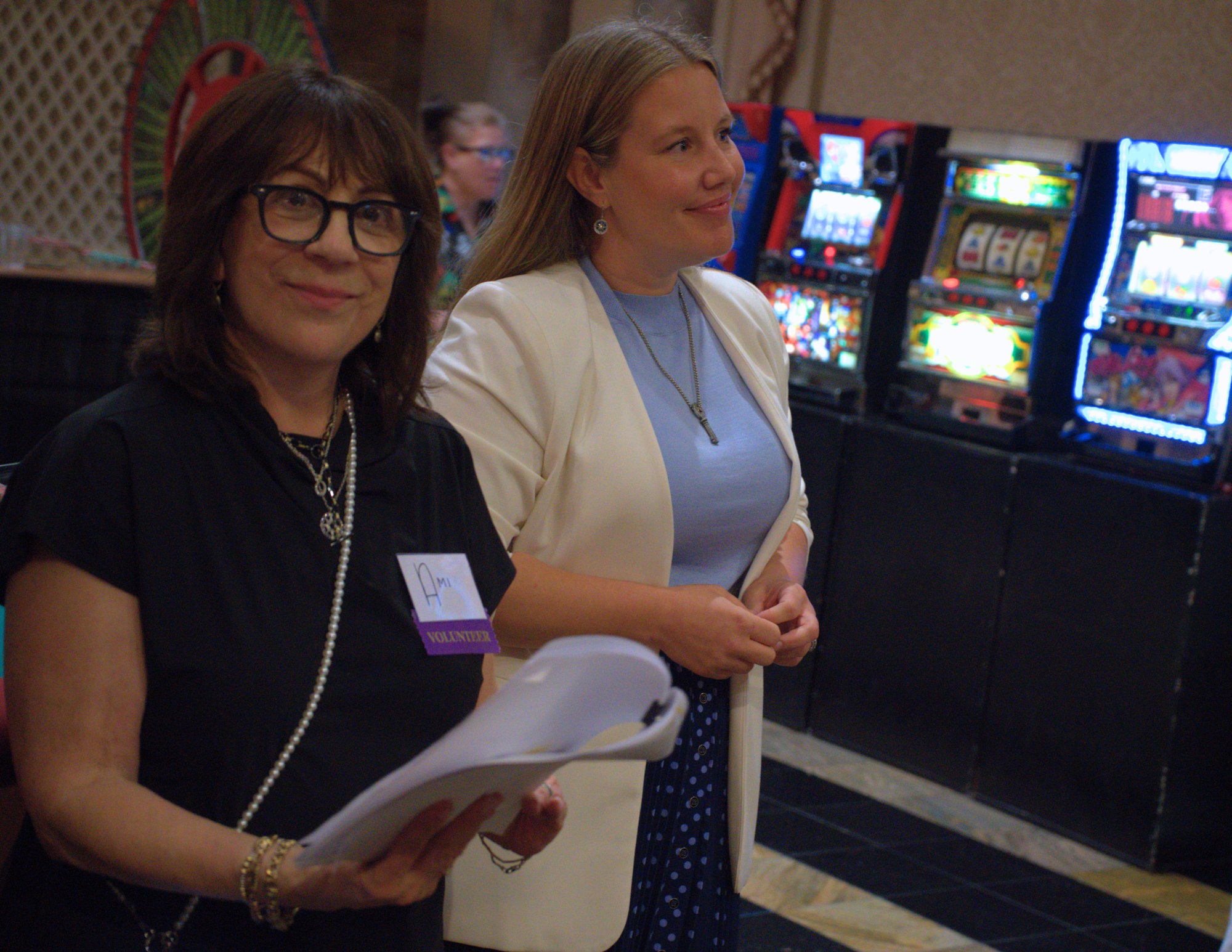 two women smiling in front of colorful slot machines.