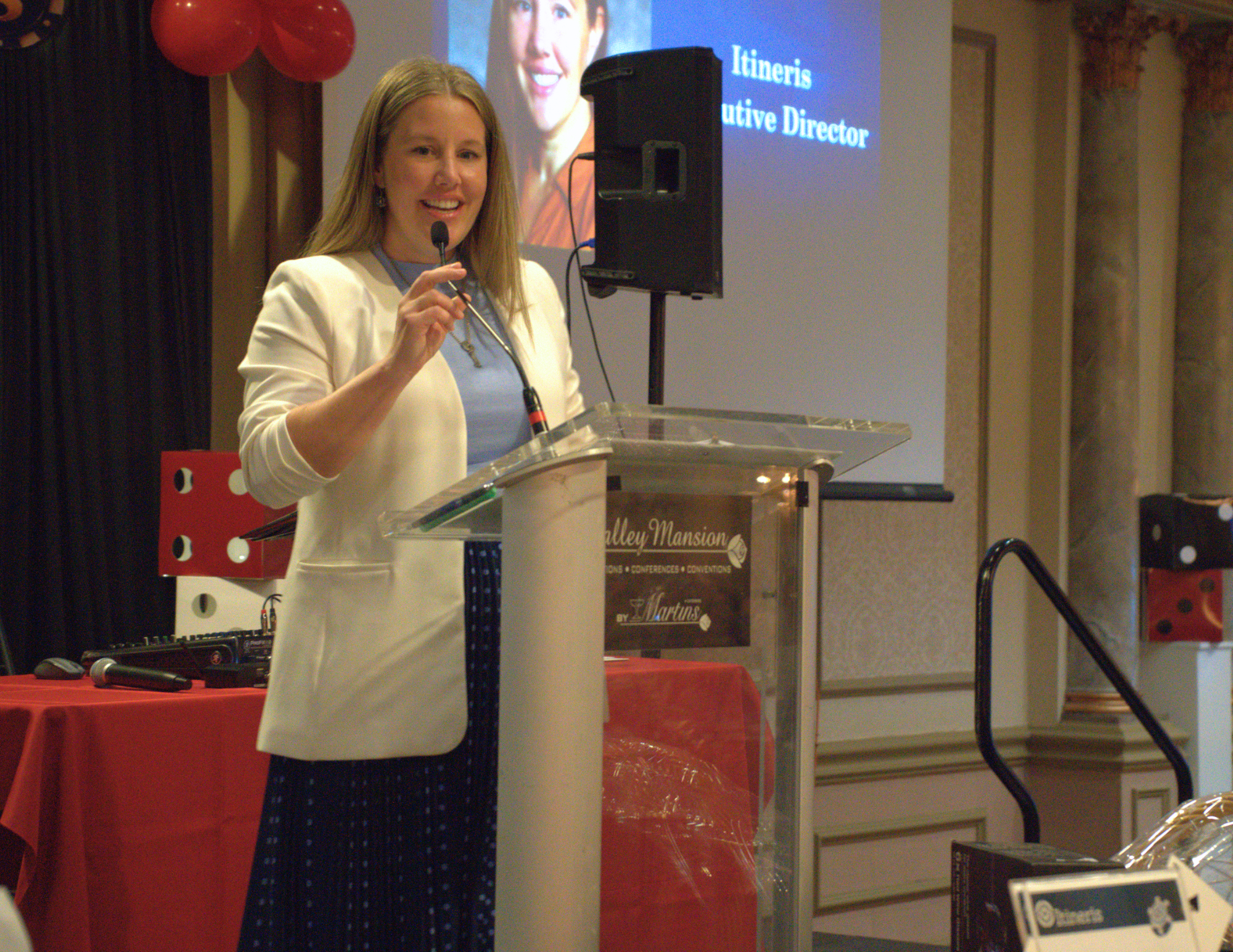 a woman in blue and white addressing a crowd with a microphone on a stage.