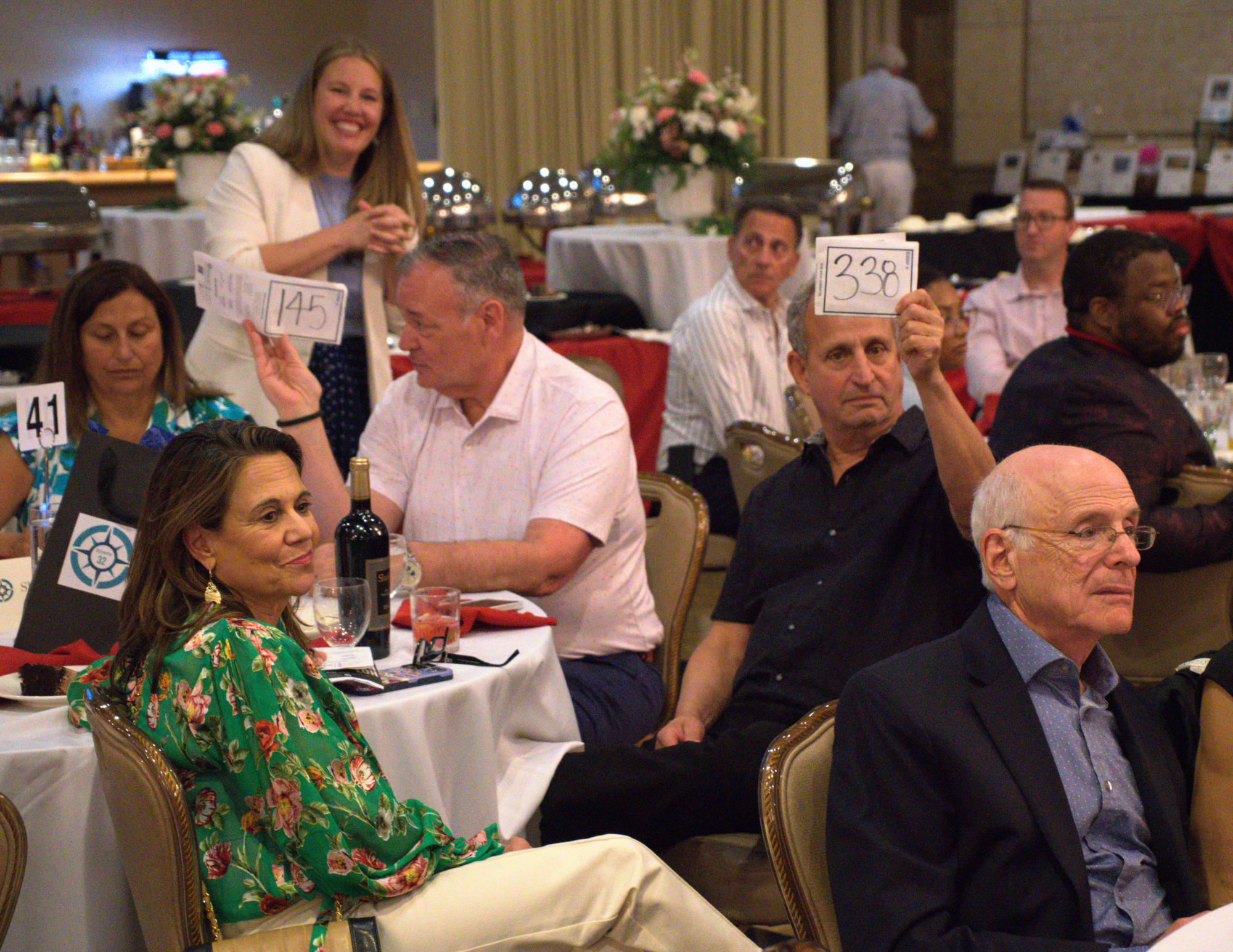 two men holding up bidder numbers while a woman standing behind them smiles.