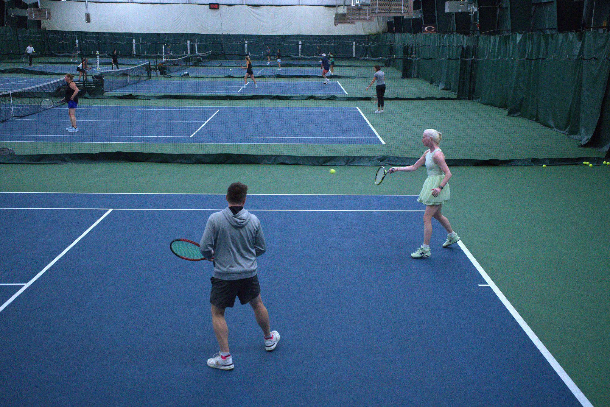 four tennis courts in a warehouse. people are playing tennis on each court.