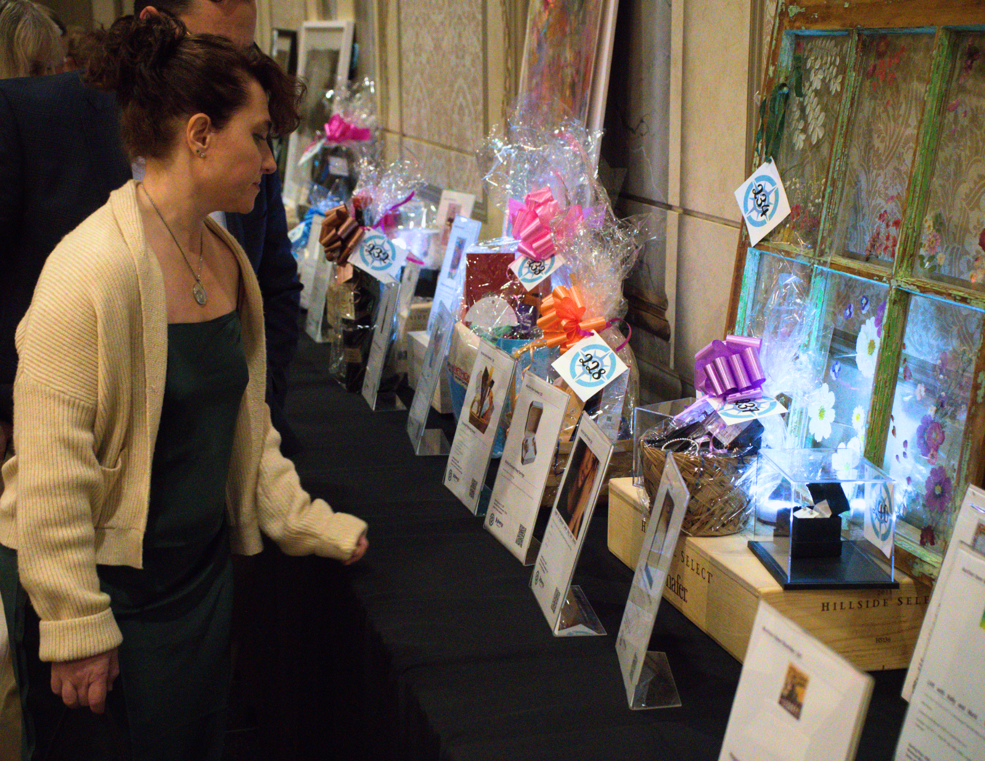 a woman in a green dress looking at silent auction items.