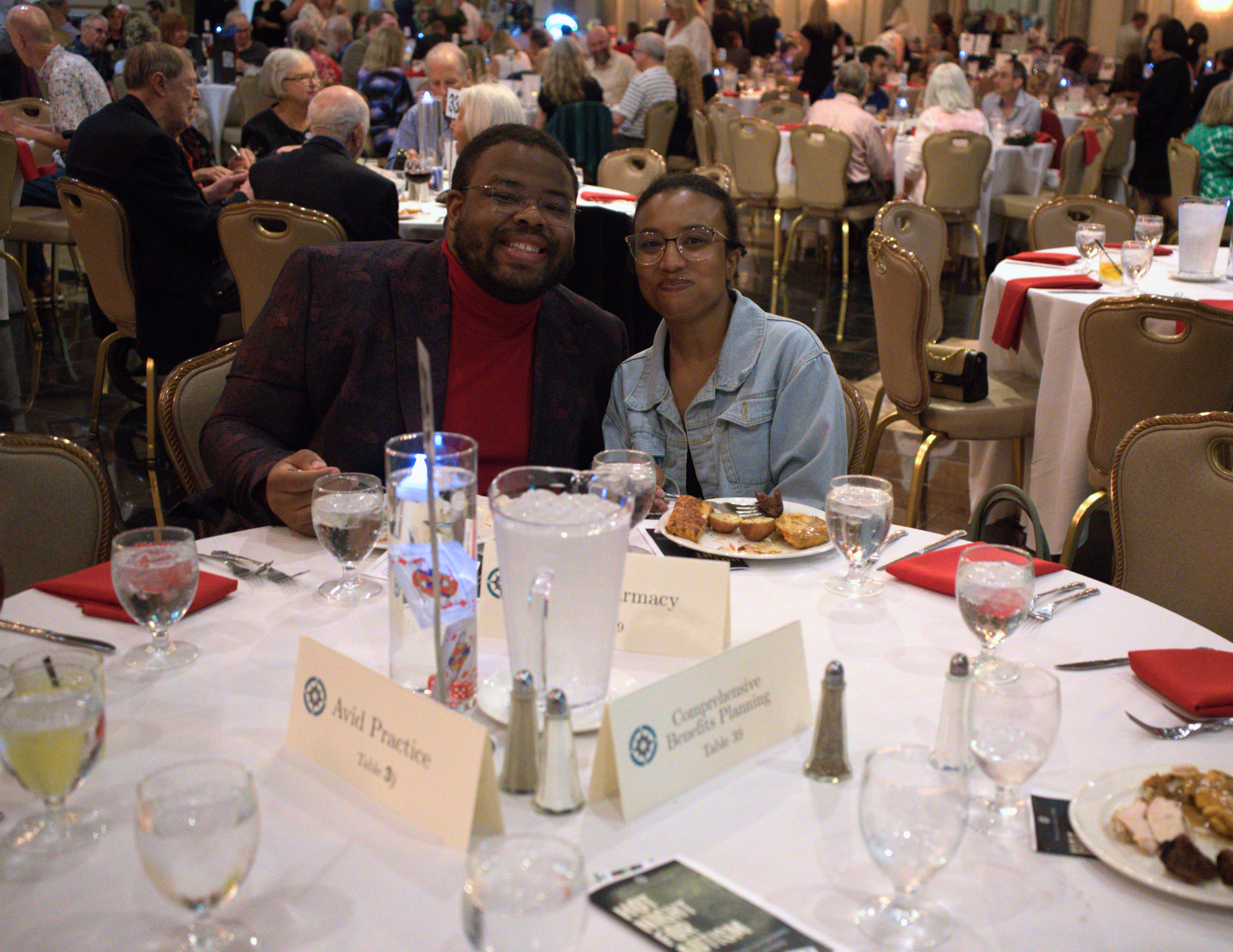 a black man and woman sitting at a dining table with a white tablecloth smiling.