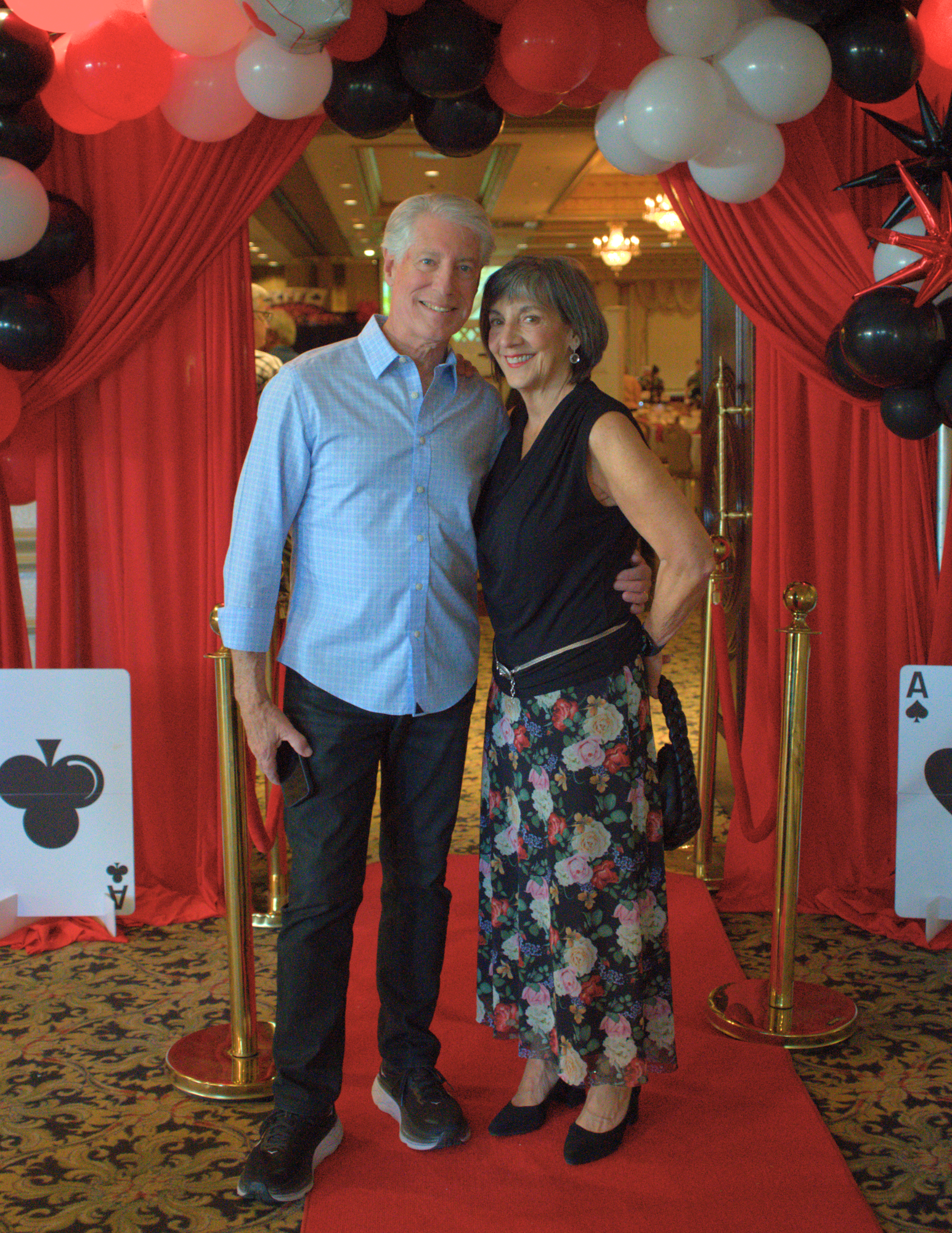 a couple dressed nicely standing in front of a red curtain with red white and black balloons.