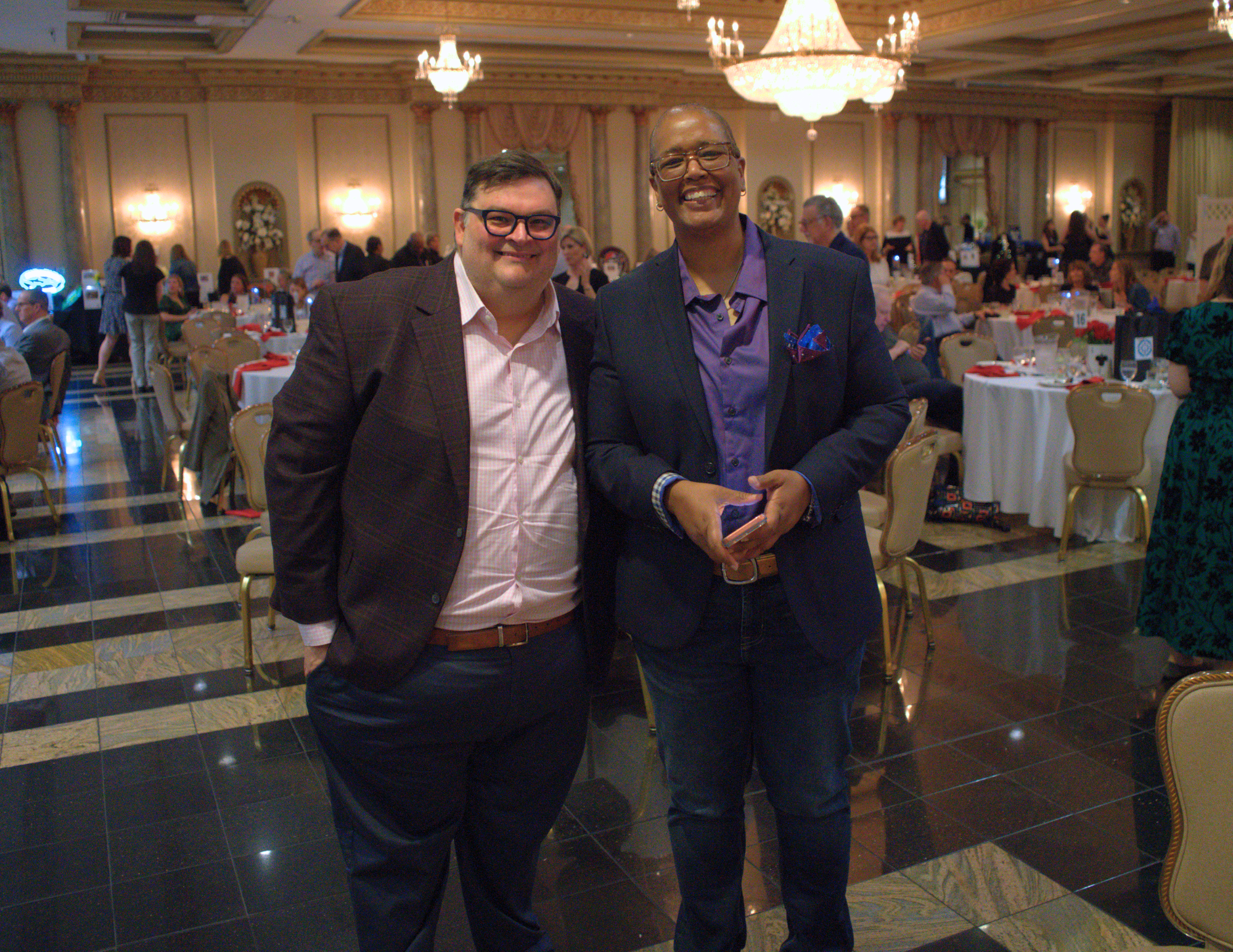 two people standing and smiling at the camera in a ballroom.