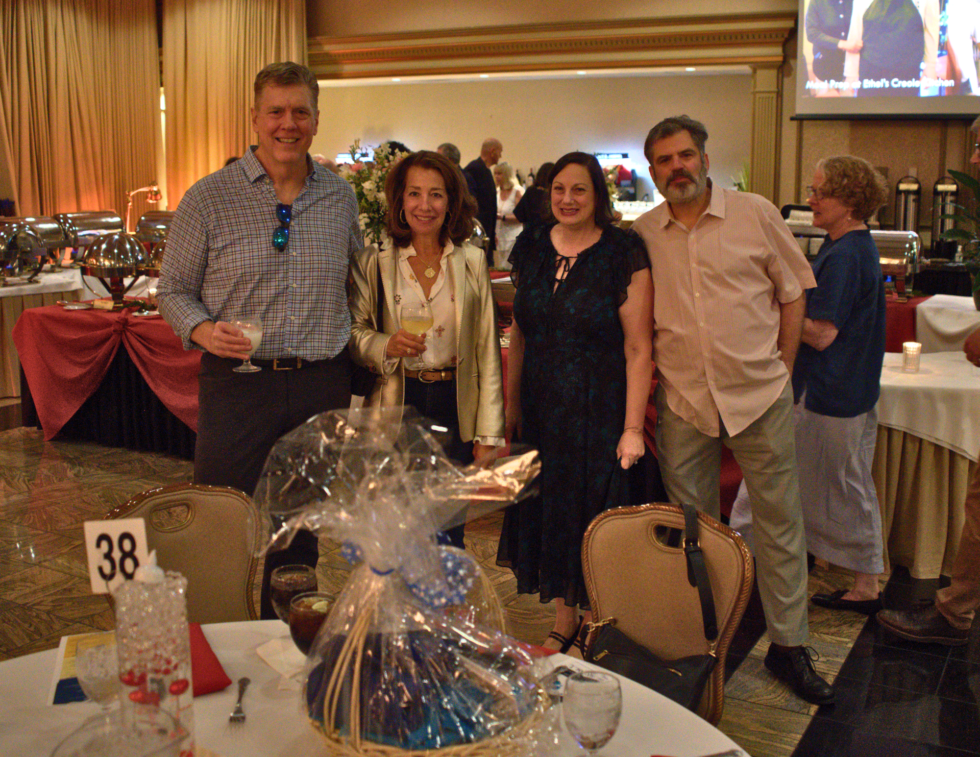 two couples holding drinks smiling in a ballroom.