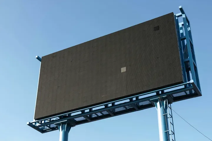Large, empty digital billboard mounted on two blue metal poles against a clear blue sky.