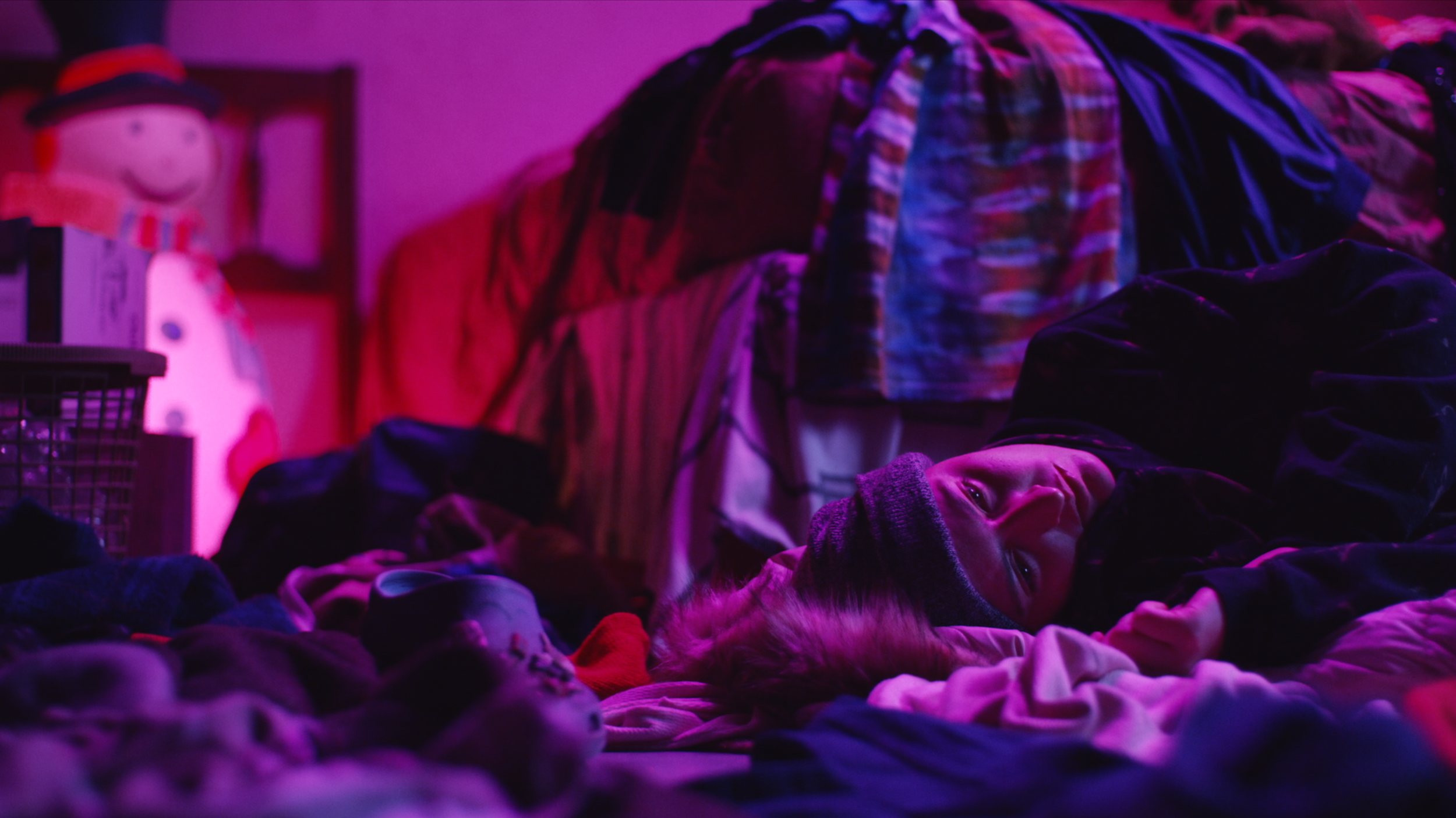 A still frame from "The Year Between": A woman lays wistfully on the floor, atop piles of laundry in her bedroom.
