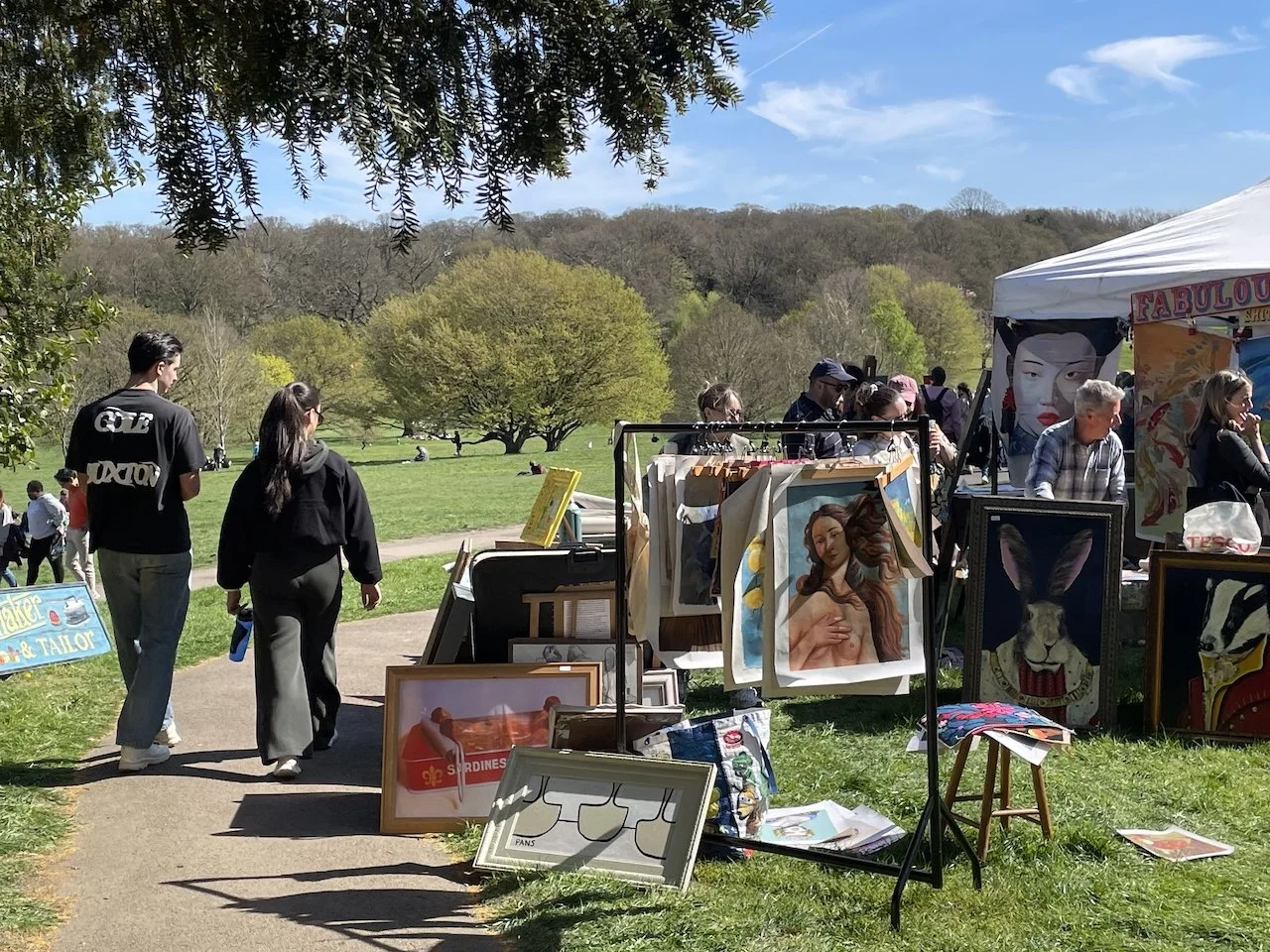 view of a vintage stallholder selling original art outside on a sunny day at So Last Century's vintage market at Beckenham Place Park, with grass and trees in the distance