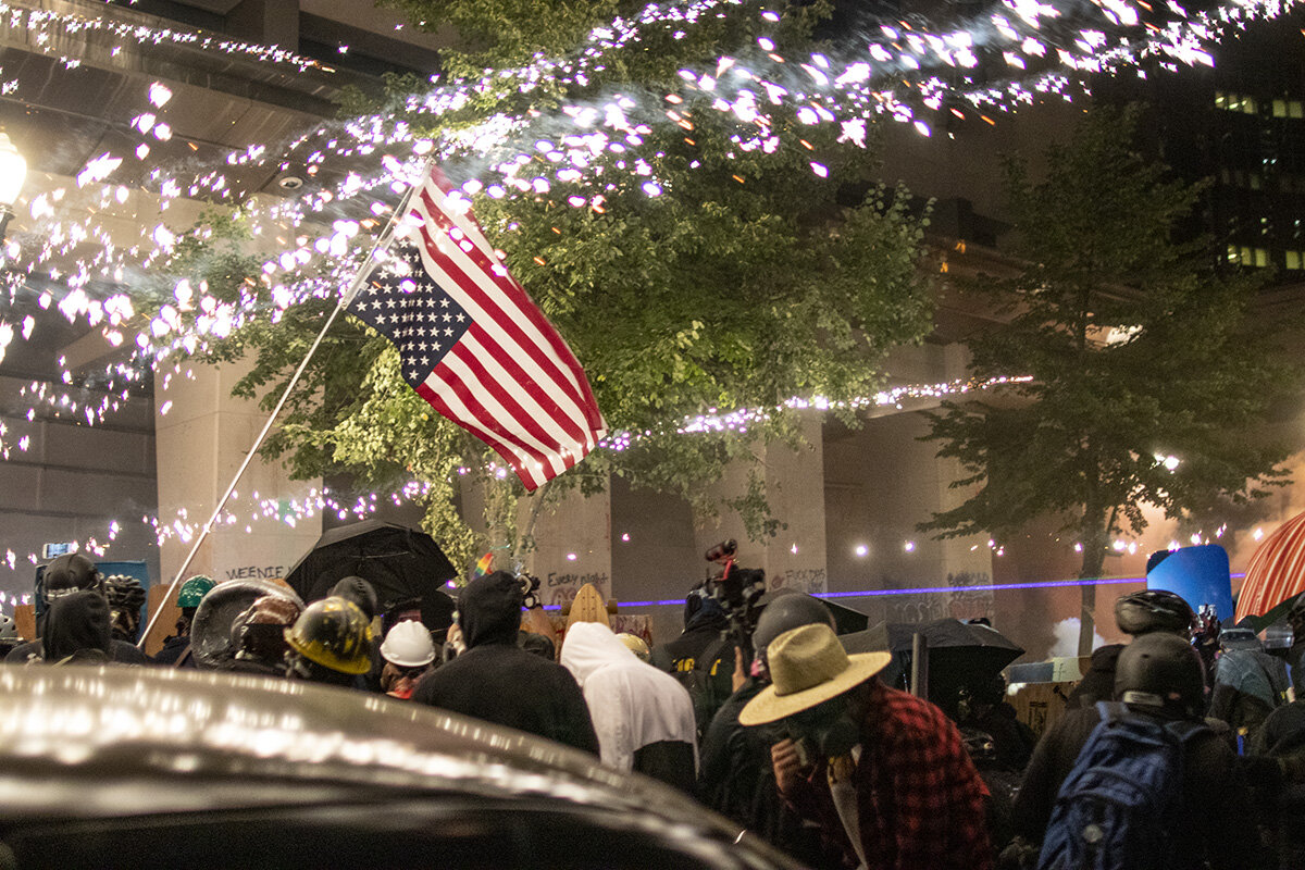  Firework sparks shooting past protesters and an upside down American flag in front of the courthouse. Approximately 3000 protesters gathered outside the Multnomah County Justice Center and the U.S. District Courthouse in downtown Portland, Oregon, o