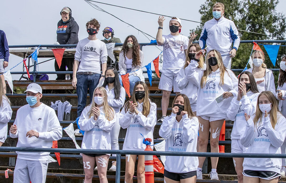  Marist high school students cheering on their team while wearing masks and practicing social distancing. On a warm, sunny Saturday afternoon, the Marist Spartans varsity football team faced off with the Marshfield Pirates for a spring home game that