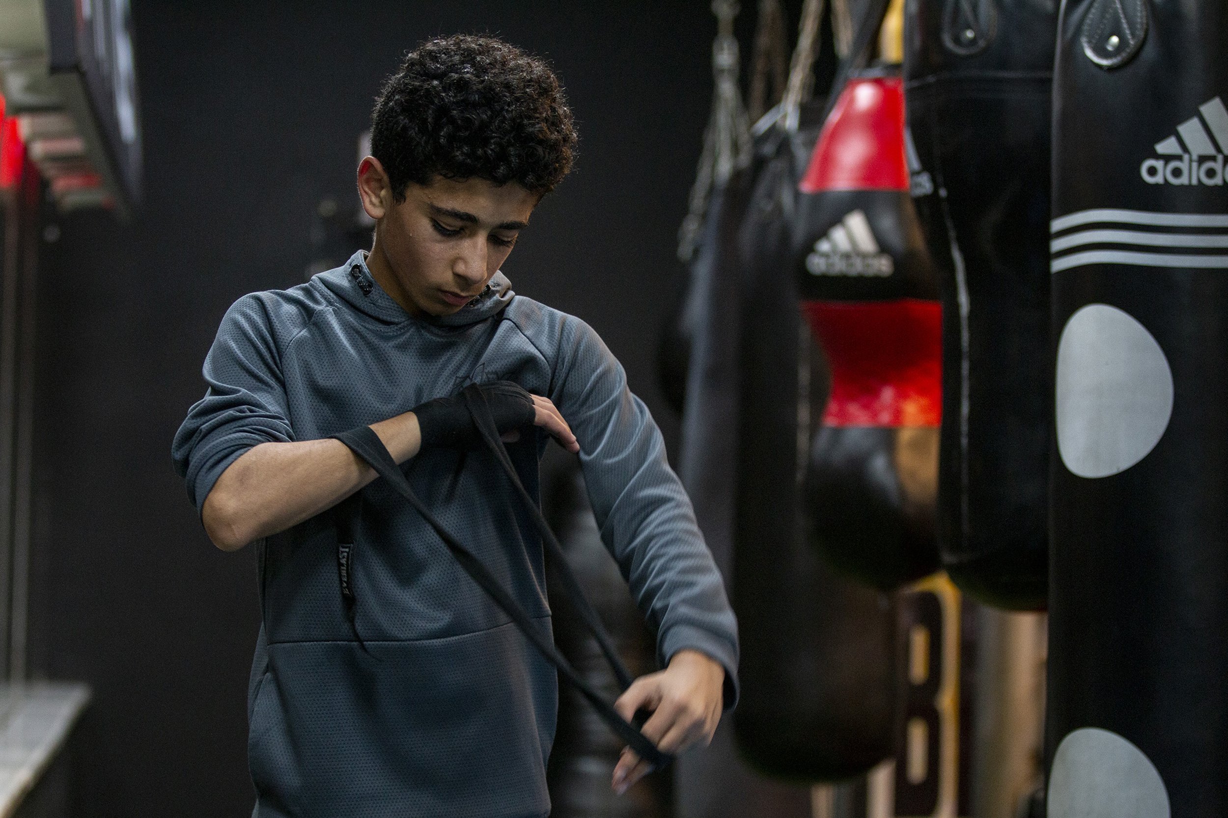 Fifteen-year-old Jaber al-Qaissi wraps his hands at the start of boxing practice at The Ring. Hand wraps in boxing are a necessity as they add support to the wrist and padding over the knuckles, helping to prevent injury.