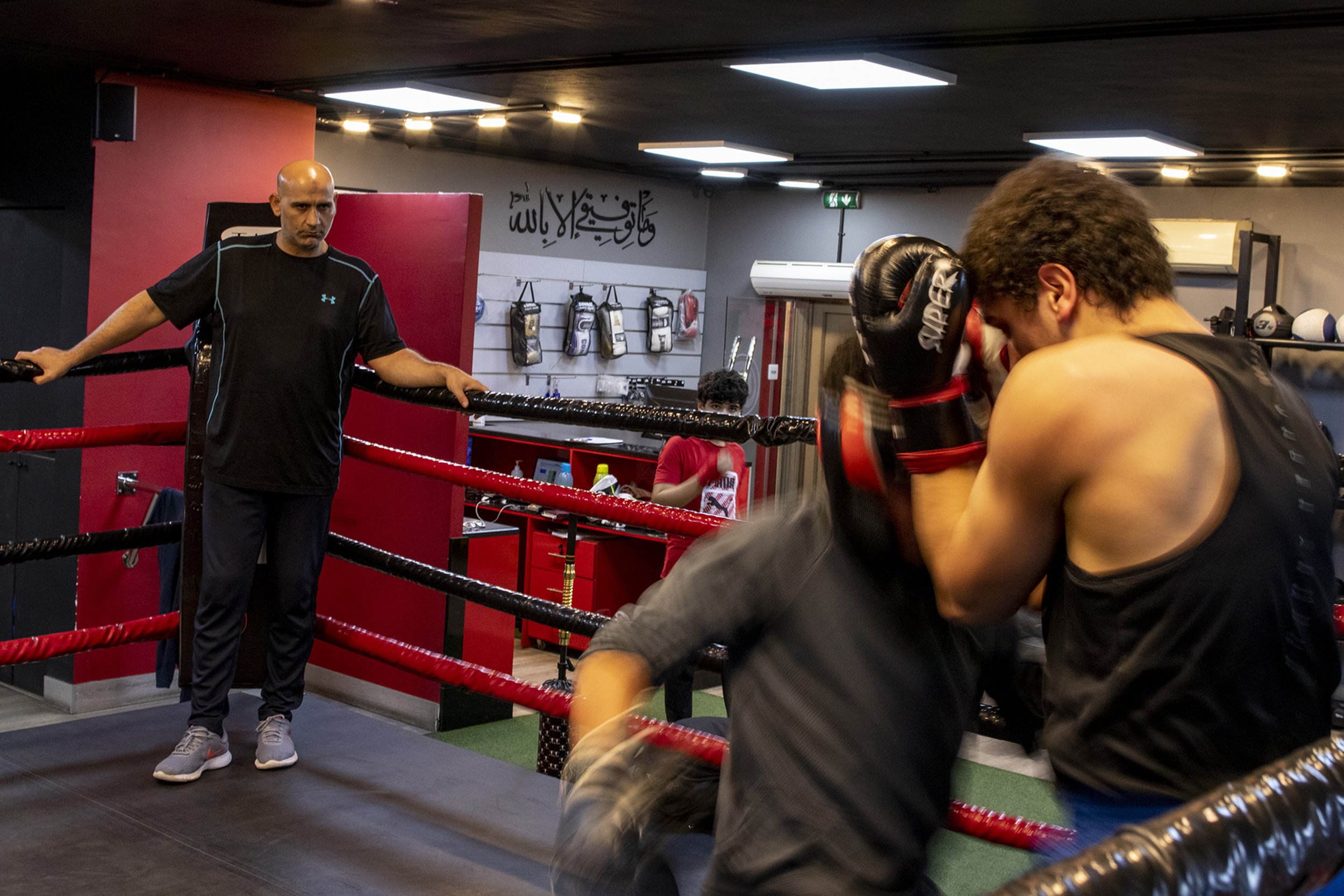 The Ring founder and head boxing coach Mohammad Ibrahim watches as al-Qaissi, left, and Mesmar, right, spar. According to Ibrahim, the Arabic calligraphy above The Ring entrance in the background translates to “my success is only by Allah.”