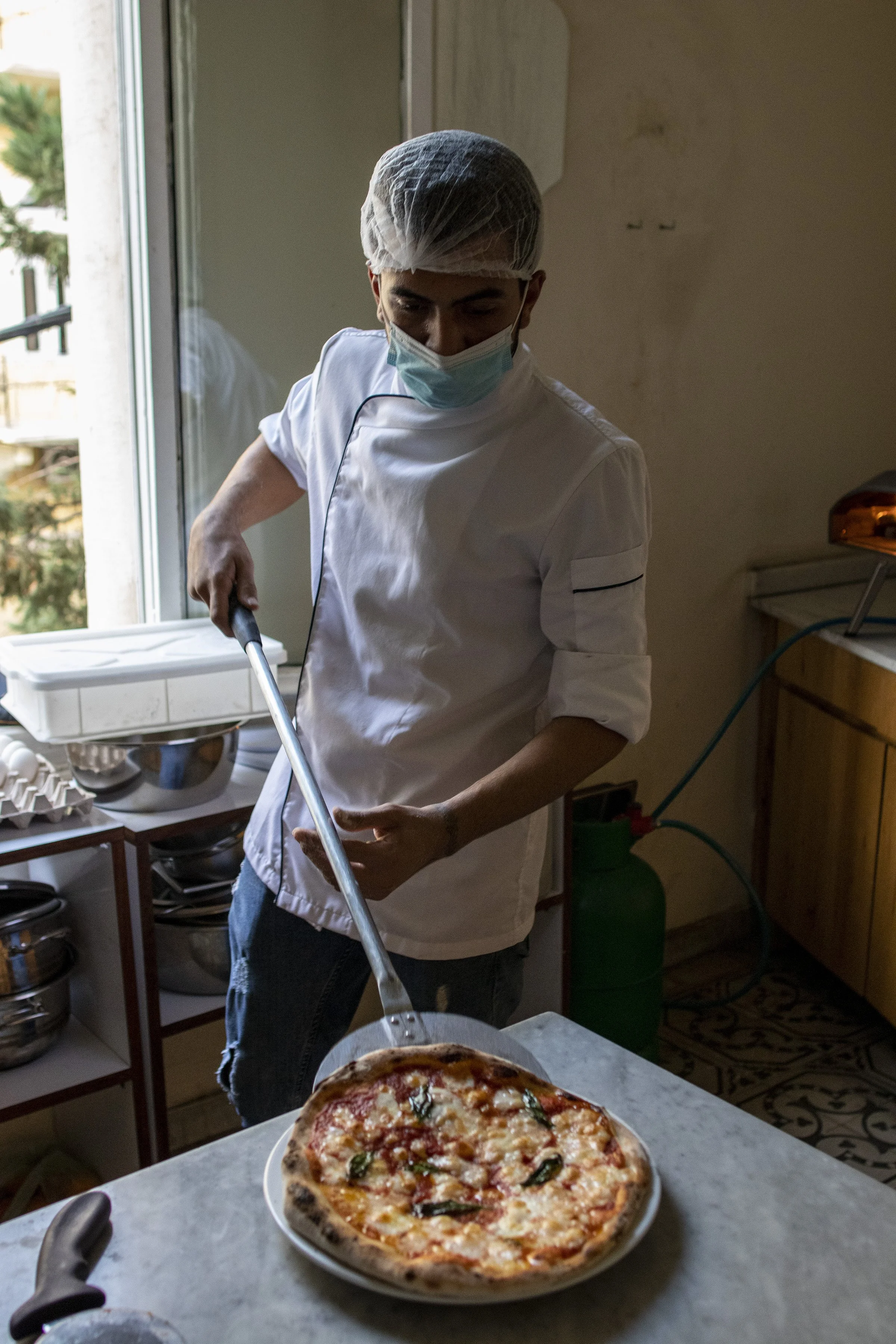  Najjar plating a finished pizza in the cafe kitchen. Pizzas are the staple on the menu, but Algelany said items previously on the menu like ice-cream had to be cut due to the power and fuel shortage. She said, “If there is a need to remove one item 