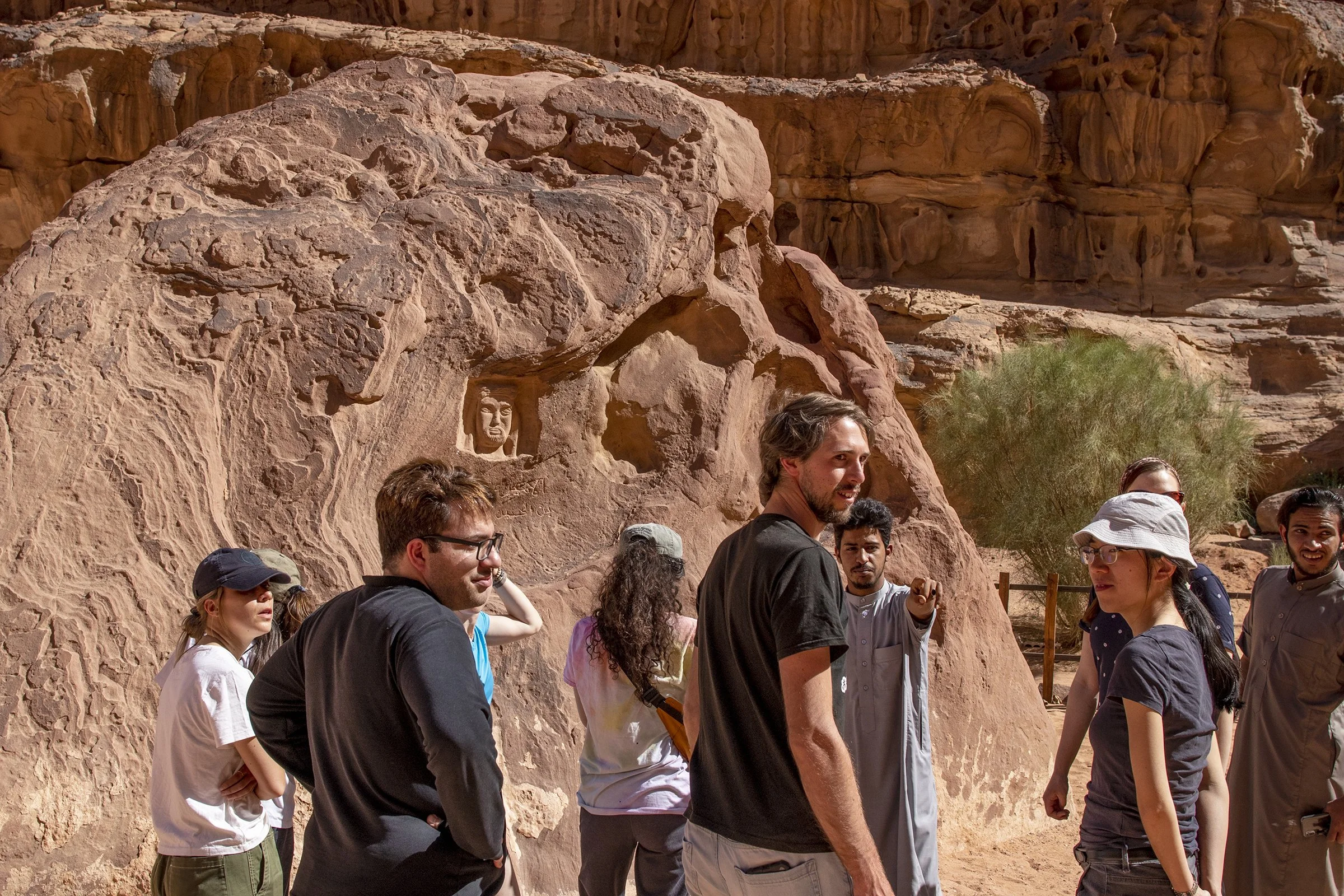  A Bedouin guide points a tourist group to a historical stone carving after explaining the history of another carving. 