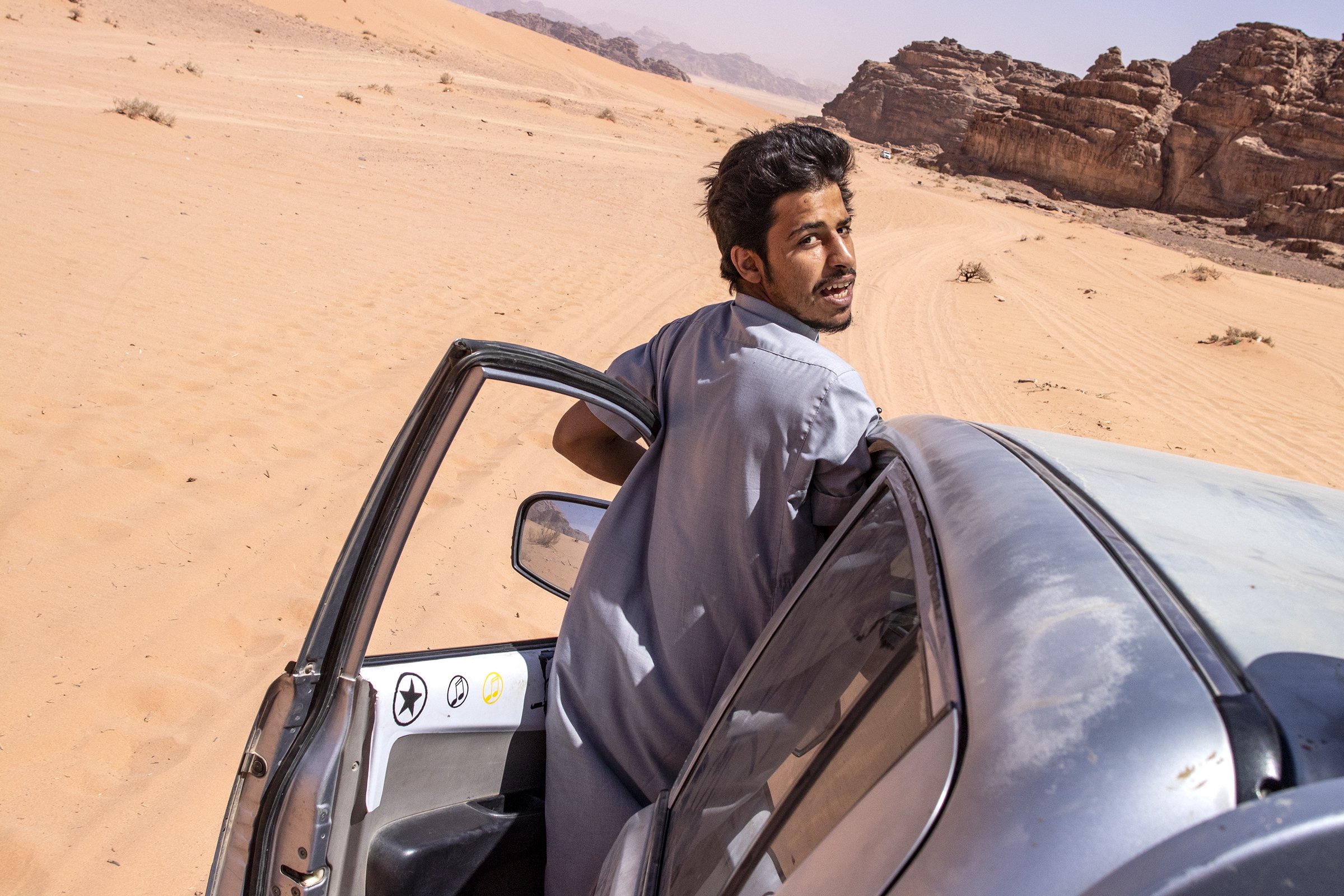  24-year-old Bedouin tribesman Mahmoad Zawayedah looking behind his shoulder while hanging outside of a truck and driving a tour group through Wadi Rum. 