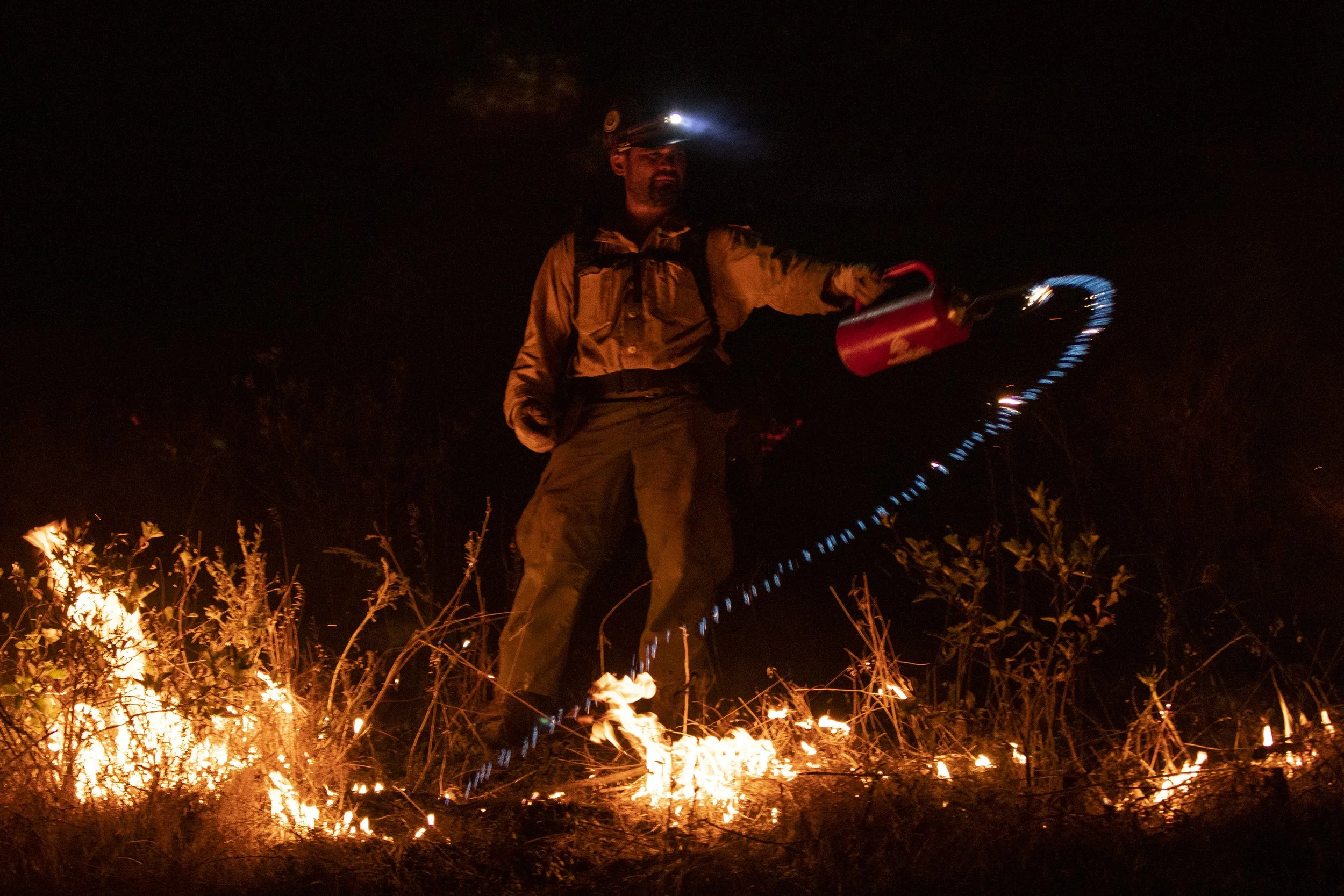 A wildland firefighter using a drip torch to light vegetation on fire during a backburn opreation. Drip torches contain a mixture of gasoline and diesel and serve as an essential tool for wildland firefighters. 