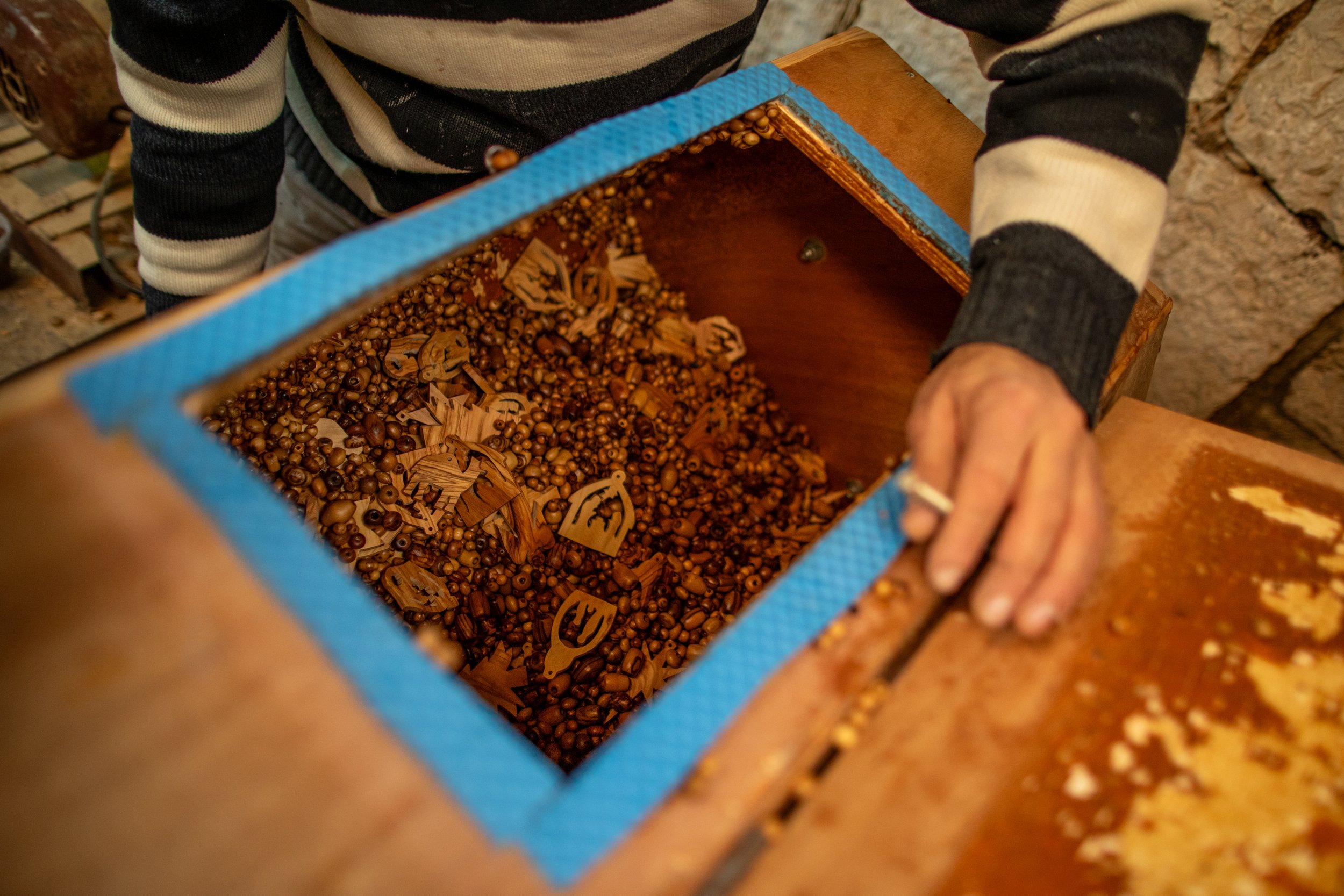  M. Giacaman collecting olive wood beads and carvings from a tumbler used to dry the wood-stained souvenirs. 