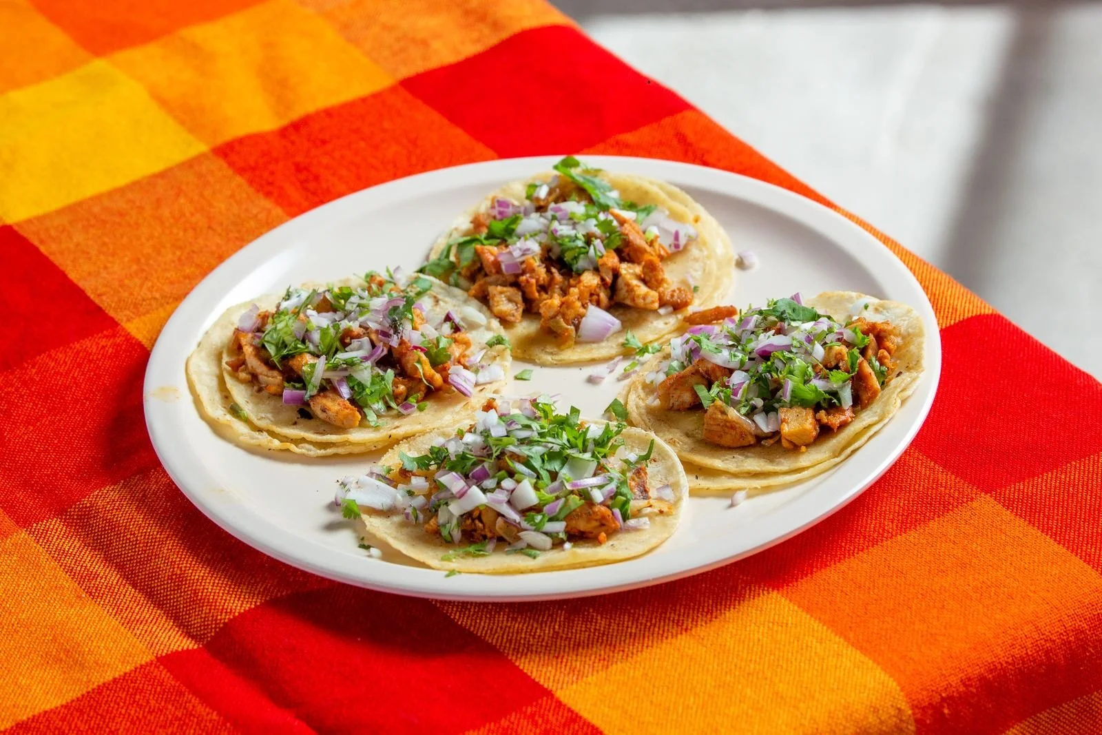 Three shredded chicken tacos on corn tortillas topped with cilantro, onion and lime wedges