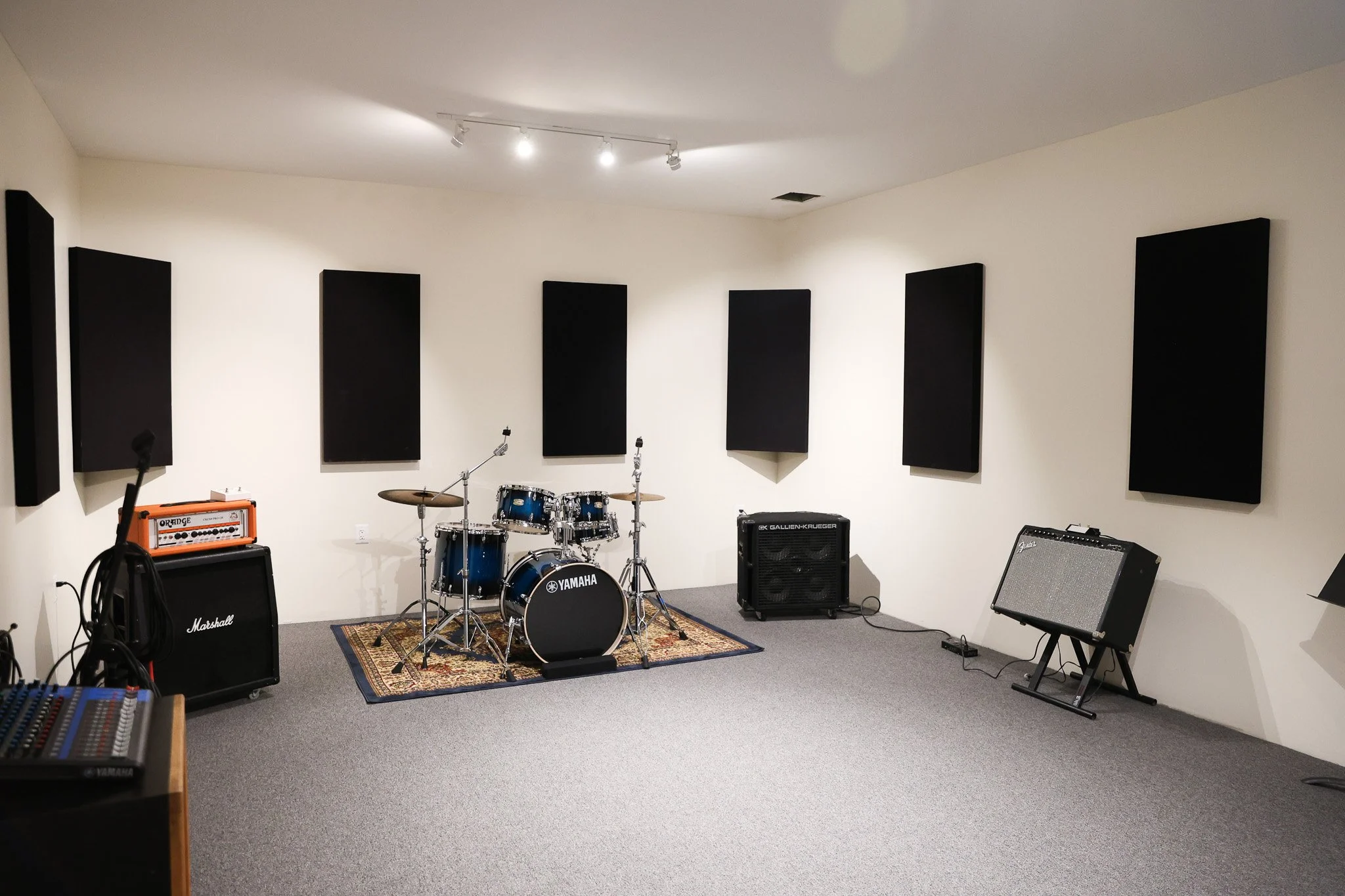 Music rehearsal room with musical instruments, speakers, and sound equipment, decorated with soundproof black panels on the white walls.