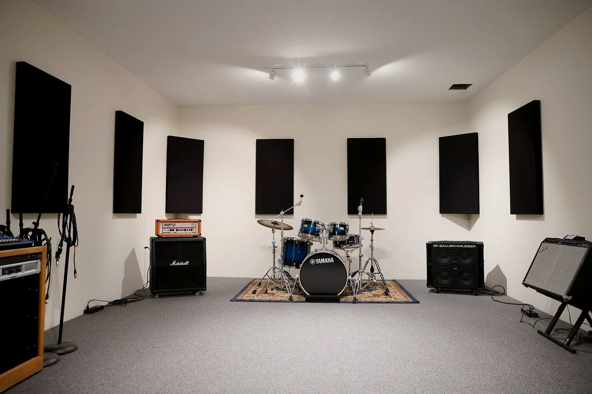 Music practice room with drum set, amplifiers, speaker, and soundproofing panels on the walls.