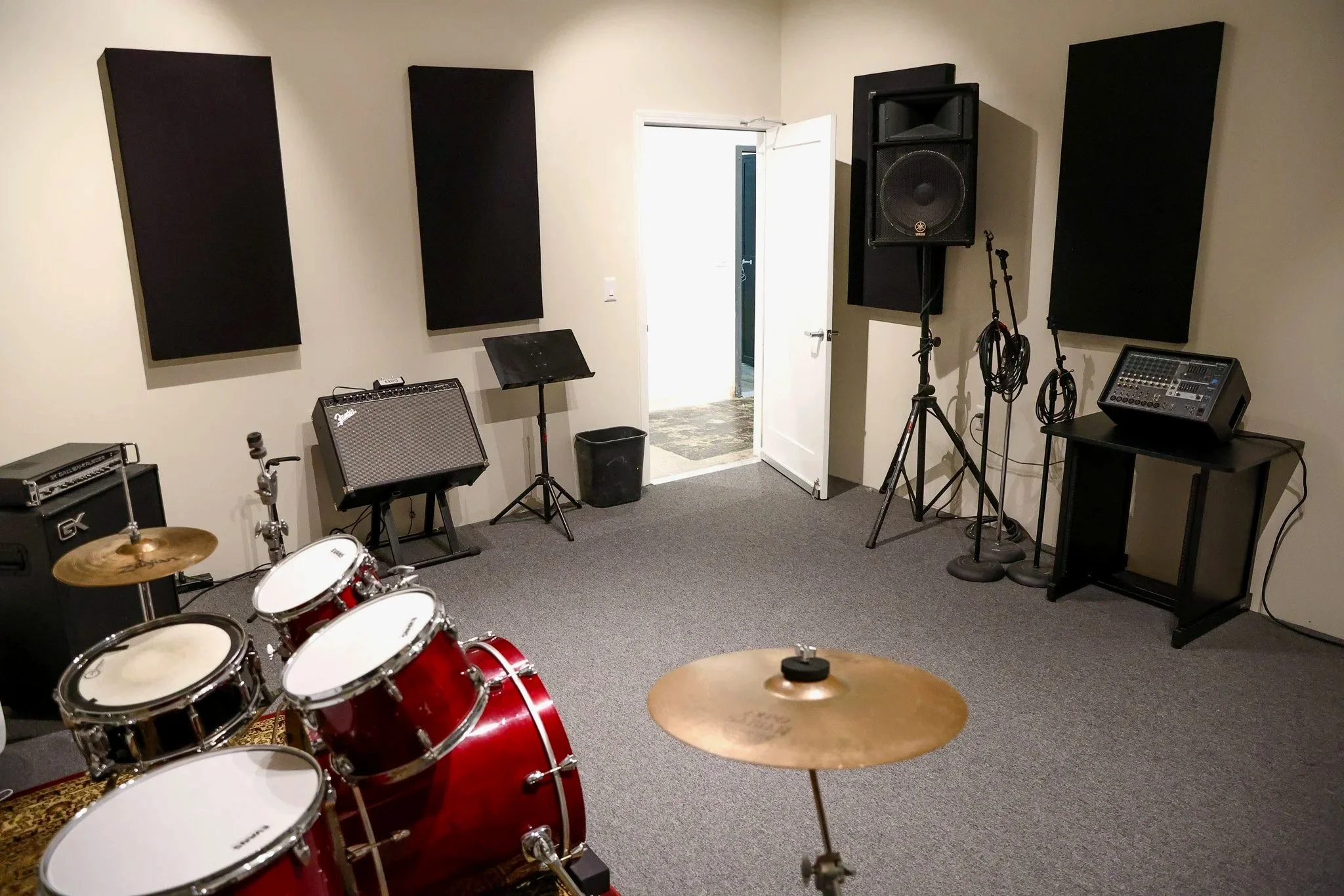 Music practice room with drums, guitar amplifier, music stand, microphone, speaker, soundproofing panels, and a door.