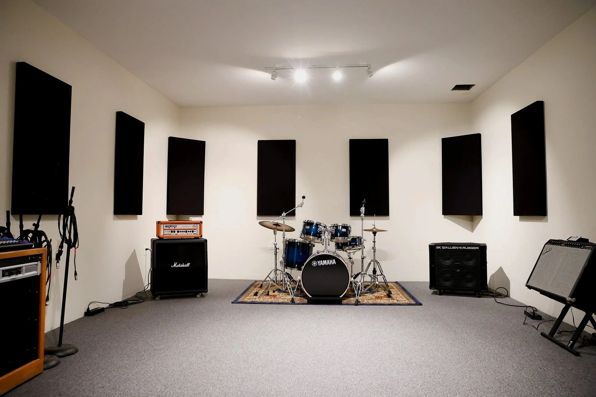 Music rehearsal room with drums, amplifiers, microphones, and soundproofing panels.