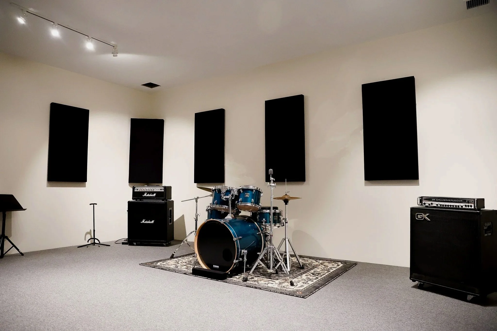 Music rehearsal room with drum set, amplifiers, and black acoustic panels on beige walls.