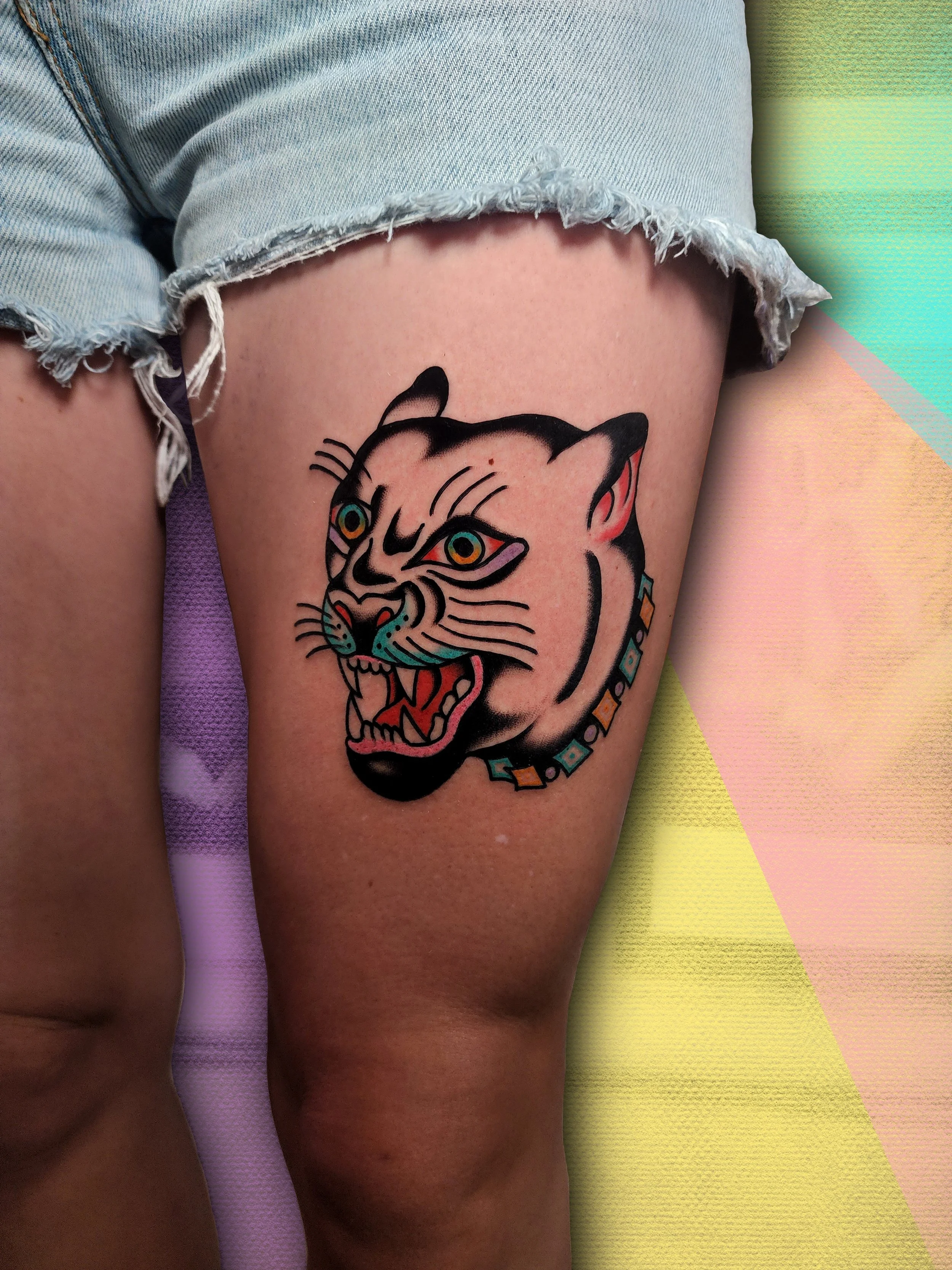 Tattoo of cat head with colorful accents, located on thigh.  