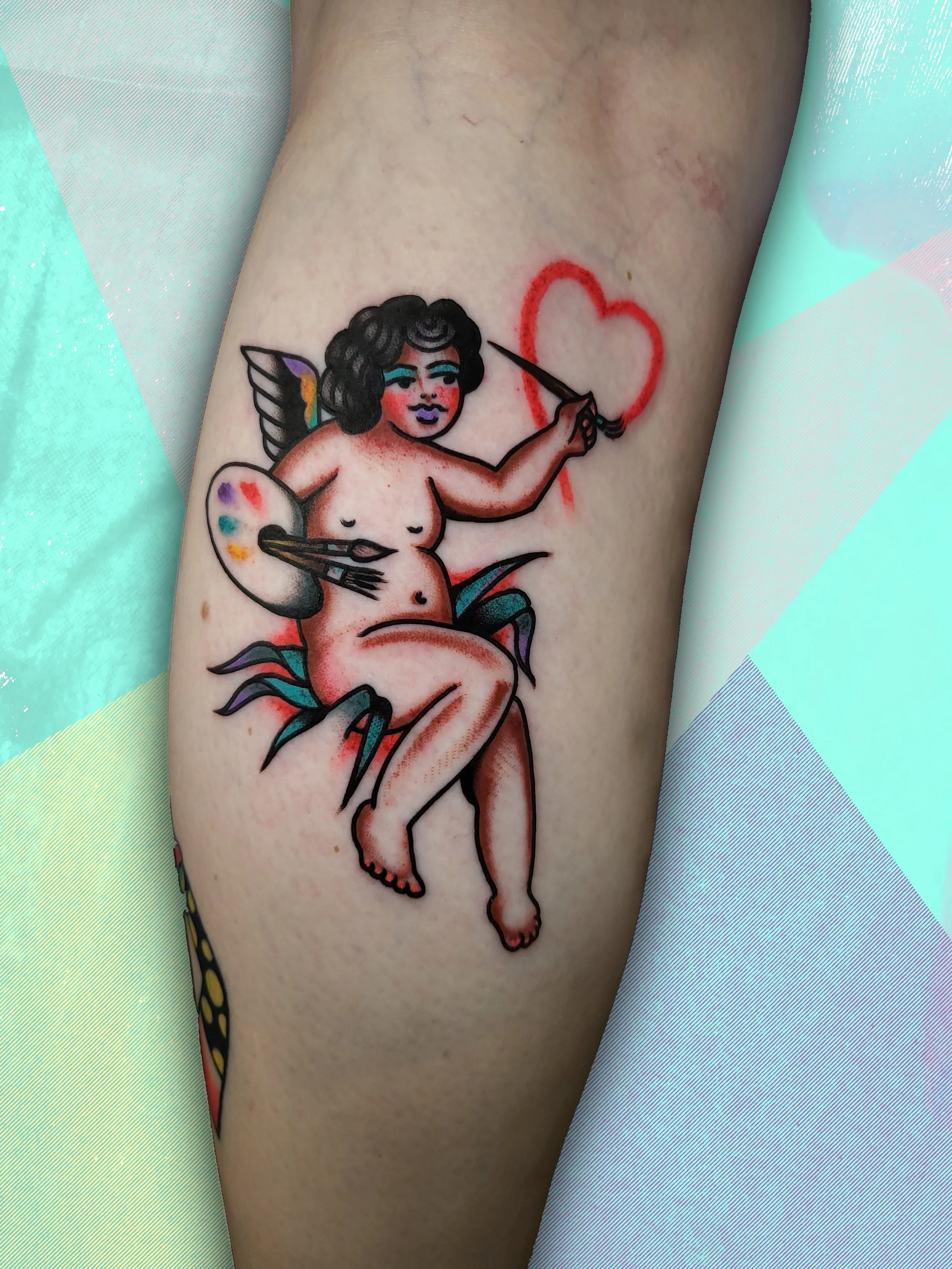  Tattoo of angel painting a heart with accents in birght colors, located  on calf.  