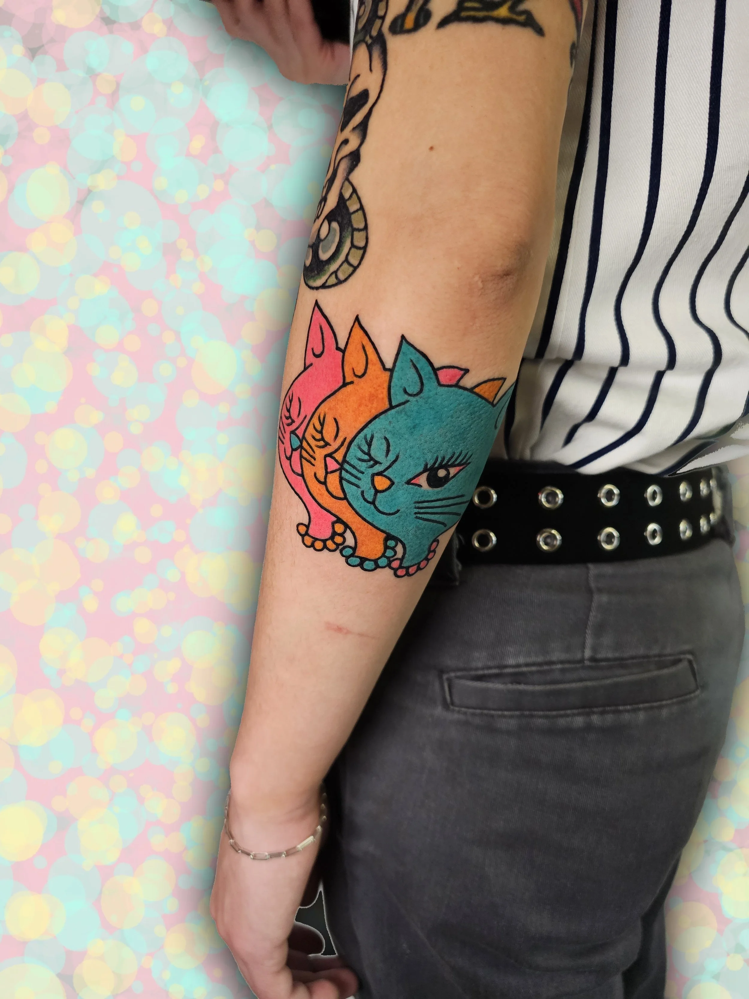  Three cartoon cats in solid colors of turquoise, orange, and pink, located on lower arm.  