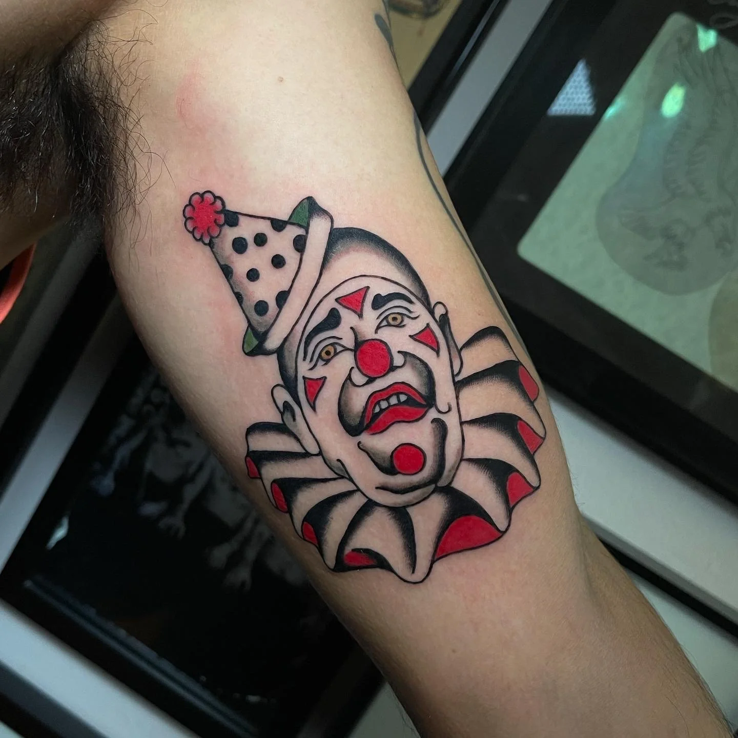  Tattoo of sad clown head with small hat and large collar on upper arm.  