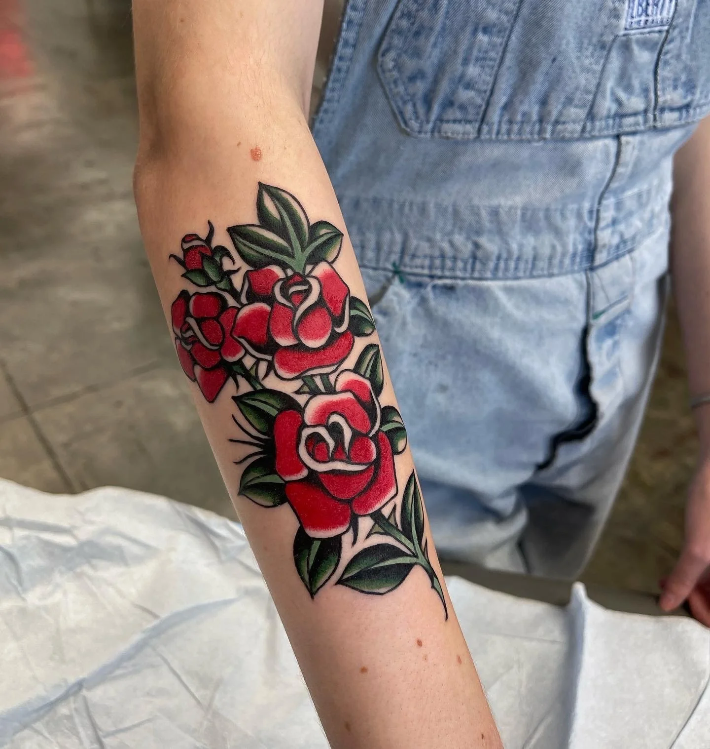  Tattoo of red roses with green leaves on lower arms.  