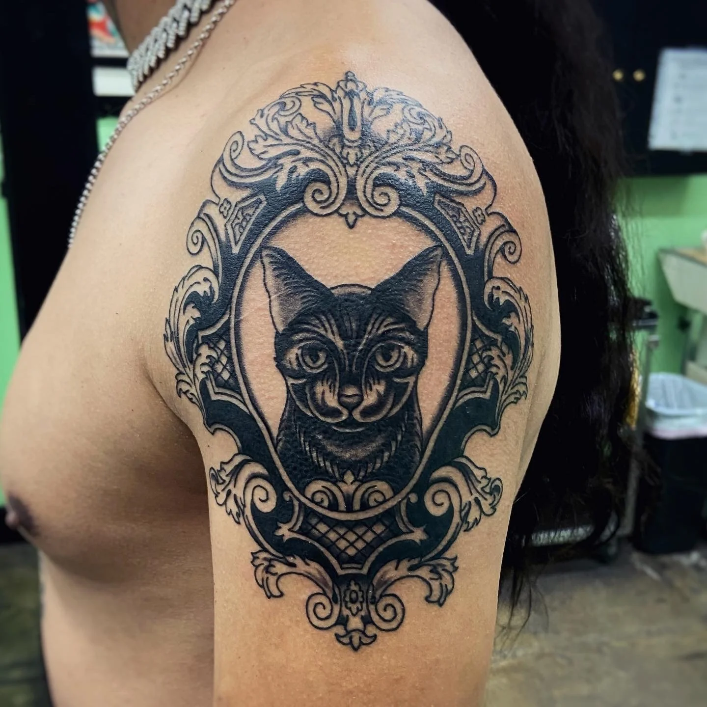Black & grey tattoo of cat inside ornate frame on upper arm