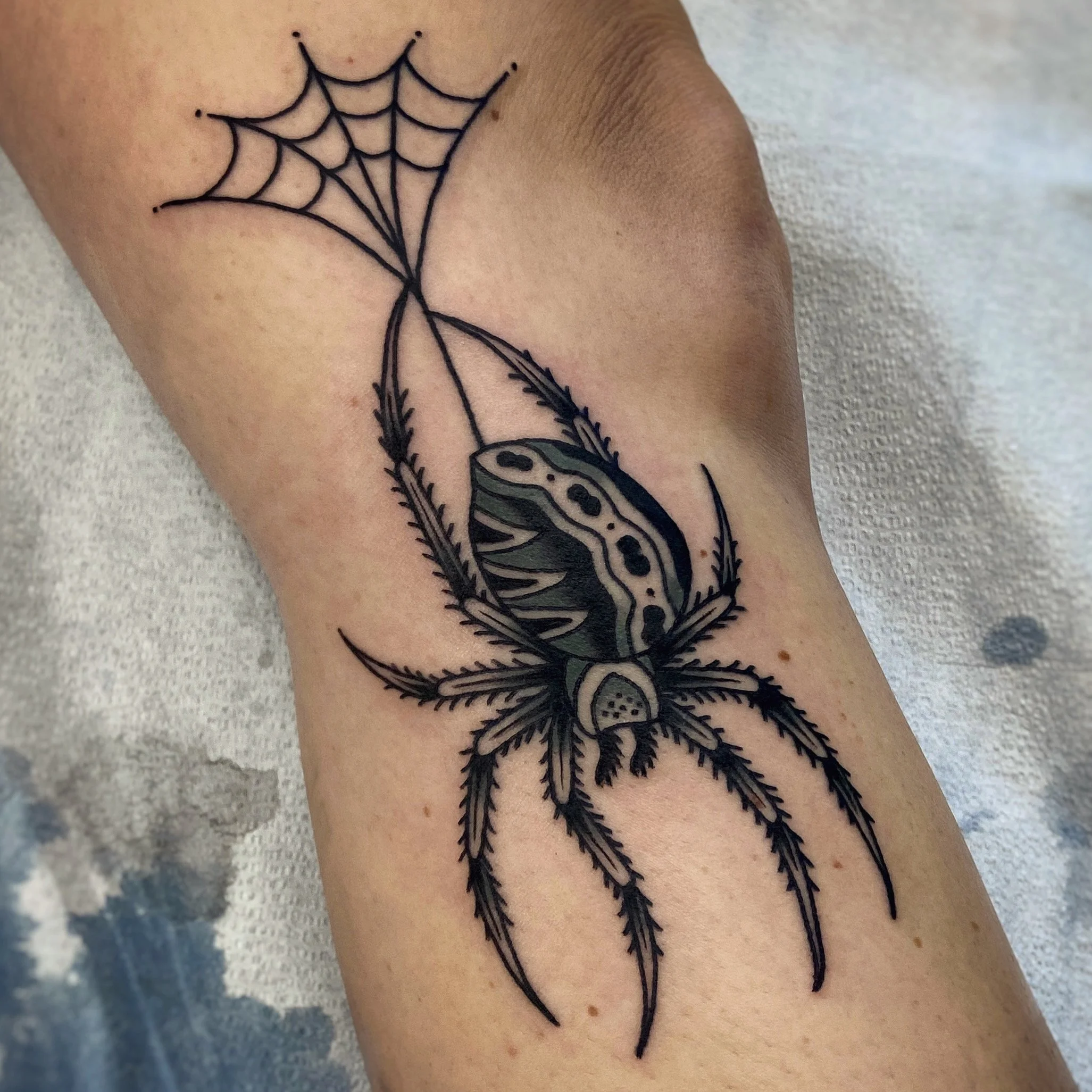 Tattoo of spider hanging from a bit of web on the side of a knee