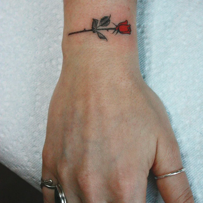 Small tattoo of long stem red rose on wrist