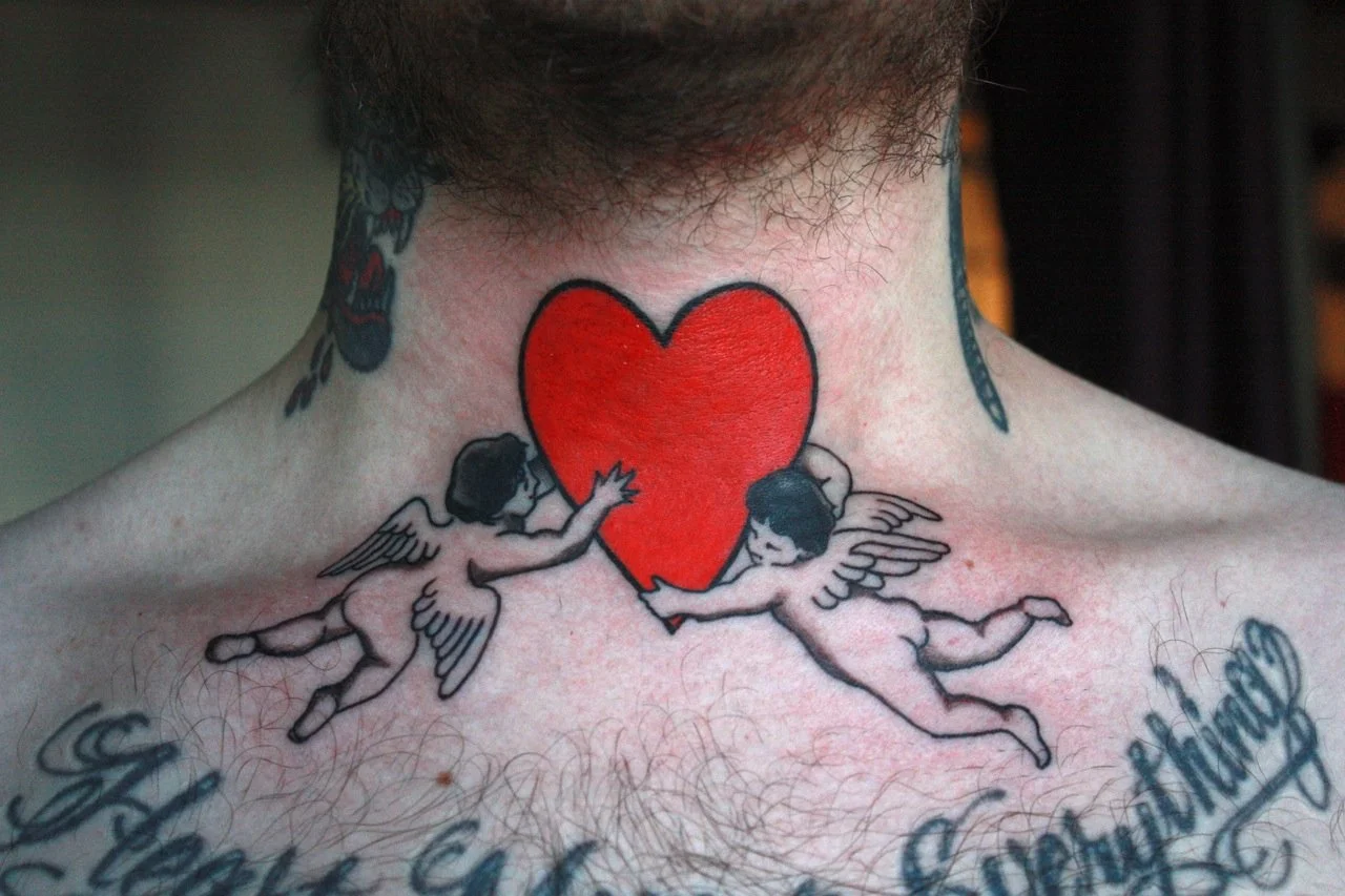 Tattoo of red heart with an angel holding it up on each side on throat