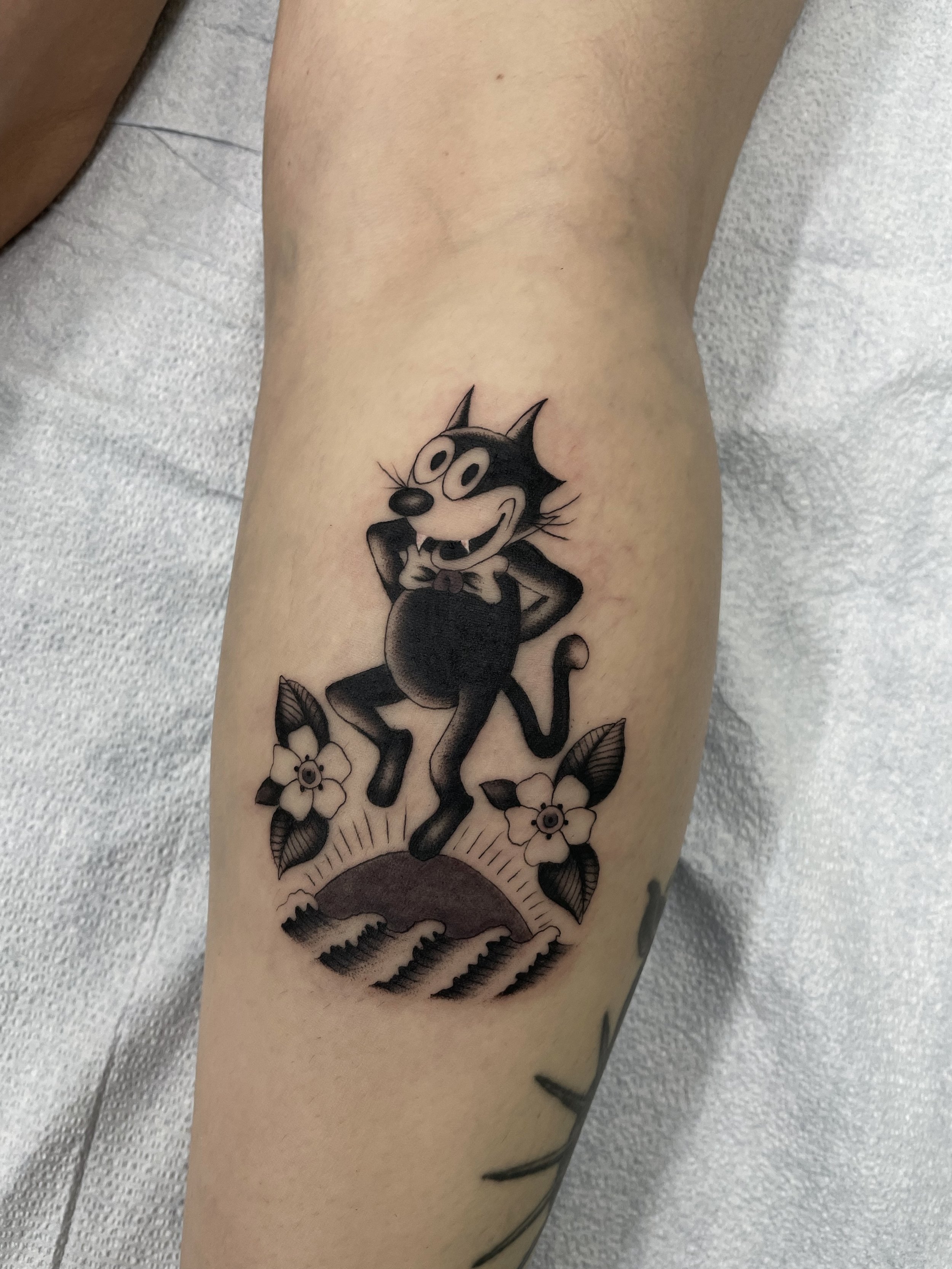 Tattoo of Felix the cat dancing, framed by two flowers
