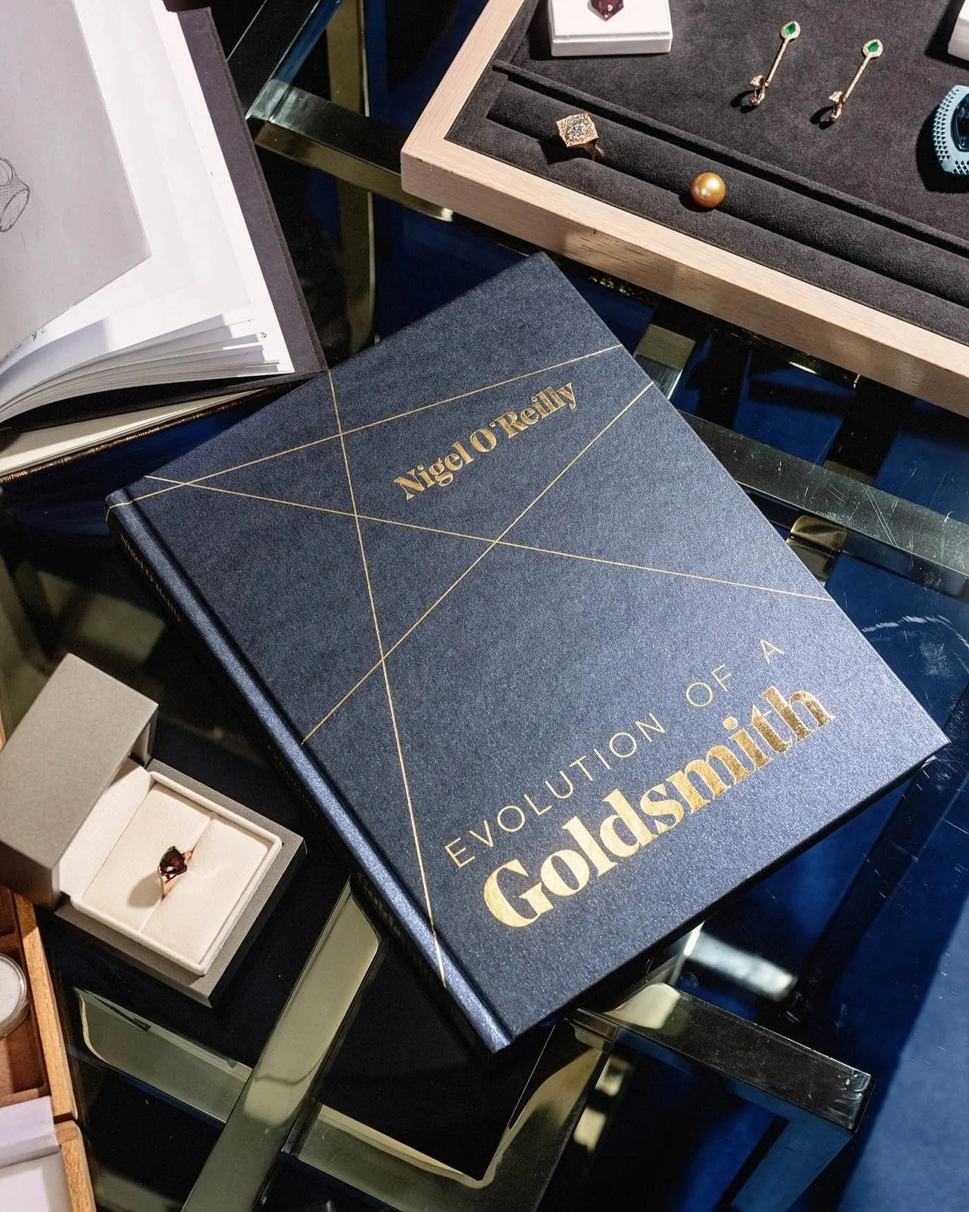 Jewellery Designer Nigel O'Reilly's book 'Evolution of a Goldsmith' sits on a table in his studio, surrounded by gemstones, sketchbooks and jewellery items