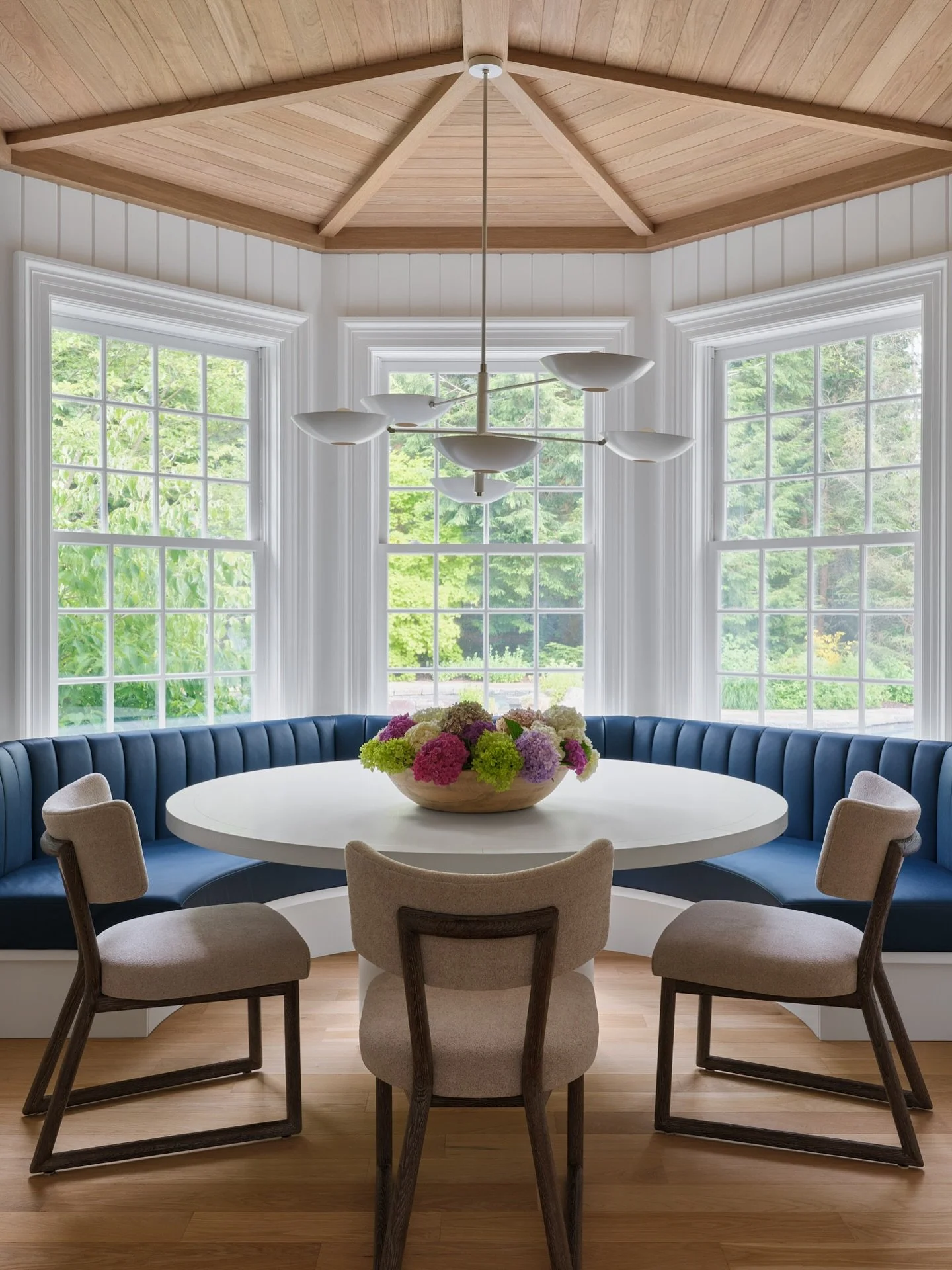 A bright breakfast nook with a custom banquette anchors the space between the kitchen and family room. Butternut planking, ceiling beams, and v-groove paneling warm and unify the rooms.