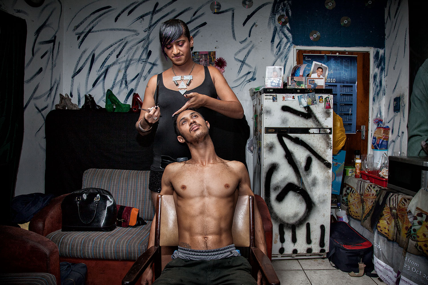  Chedino cuts the hair of a friend at Miss Whall’s house, Ravensmead, Cape Town, 2014.   Aside from her job in a call center, Chedino worked as a hairdresser to earn some extra money. 