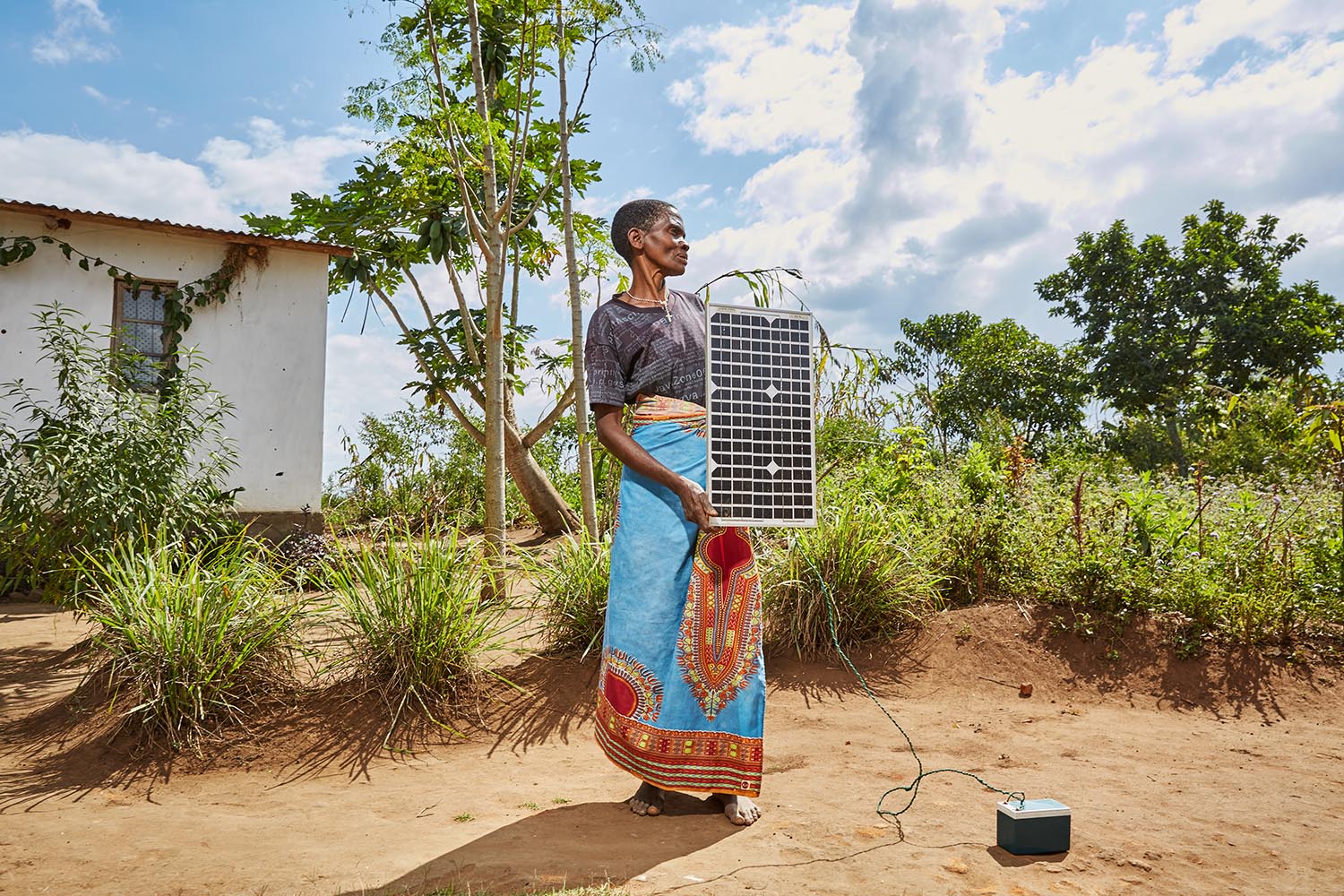  Violet Napazi, 57, holds up the solar panel owned by her son, Luchenza, Malawi, 2017.  Charging mobile phones is becoming a profitable business, especially since solar panels are becoming cheaper to buy and build. Until recently, Violet’s family use