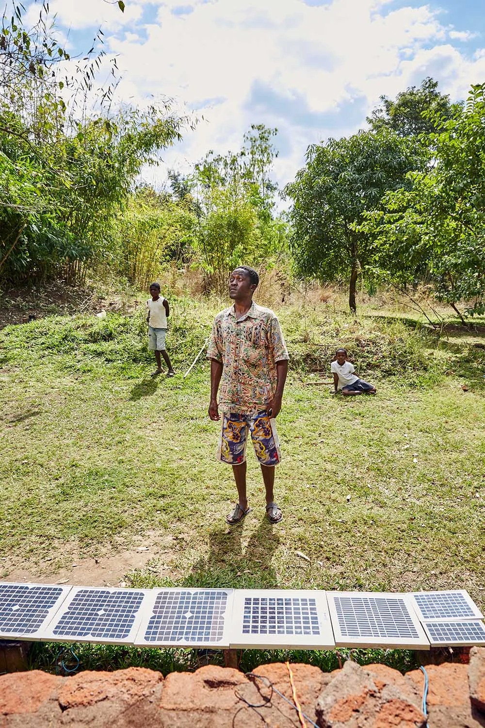 Felix Wonga (29) waits for the sun to appear from behind a cloud, Luchenza, southern Malawi, 2017. Customers pay up to 50 Kwatcha (7 cents) to charge their phones using the electricity generated by Felix’s solar panels. Felix is saving to buy a set of bigger panels that provide enough power to ensure a continuous supply of electricity. With his current panels, if the sun is blocked by a cloud, the power stops.