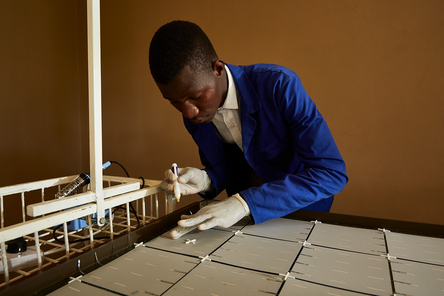  Thomas, a student at Green Malata, an entrepreneurial village, carefully solders metal strips to the back of a solar panel, Luchenza, Malawi, 2017.  Thomas and his fellow students are part of Green Malata’s Renewable Energy course, during which they