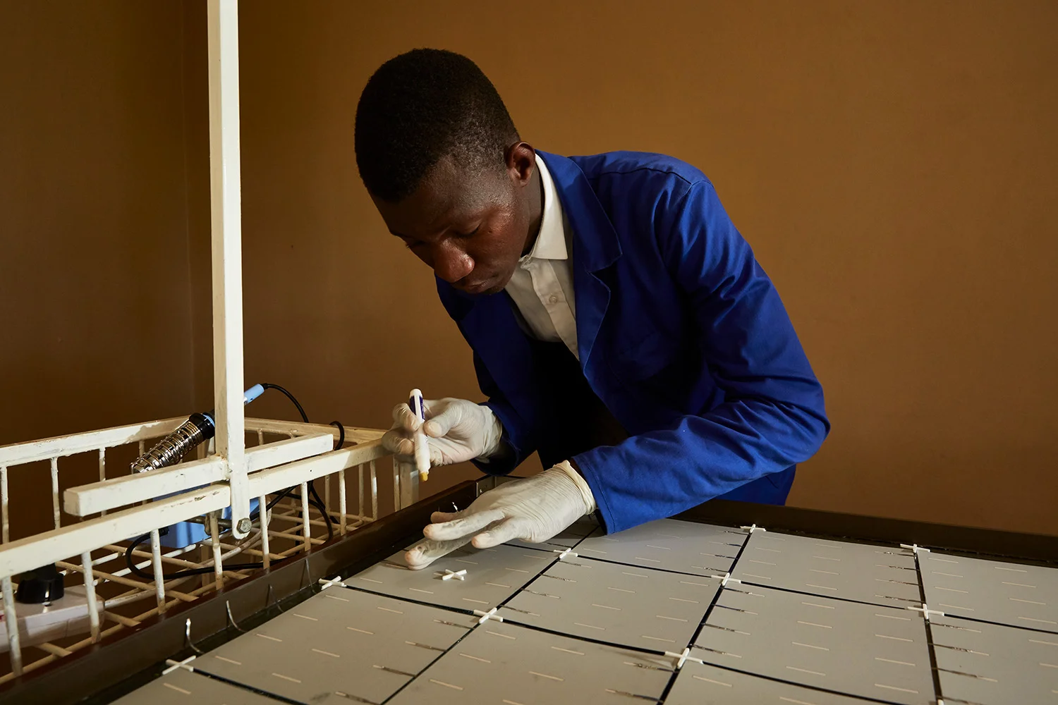 Thomas, a student at Green Malata, an entrepreneurial village, carefully solders metal strips to the back of a solar panel, Luchenza, southern Malawi, 2017. Thomas and his fellow students are part of Green Malata’s Renewable Energy course, during which they learn about a range of different green alternatives to on-grid electricity generation.