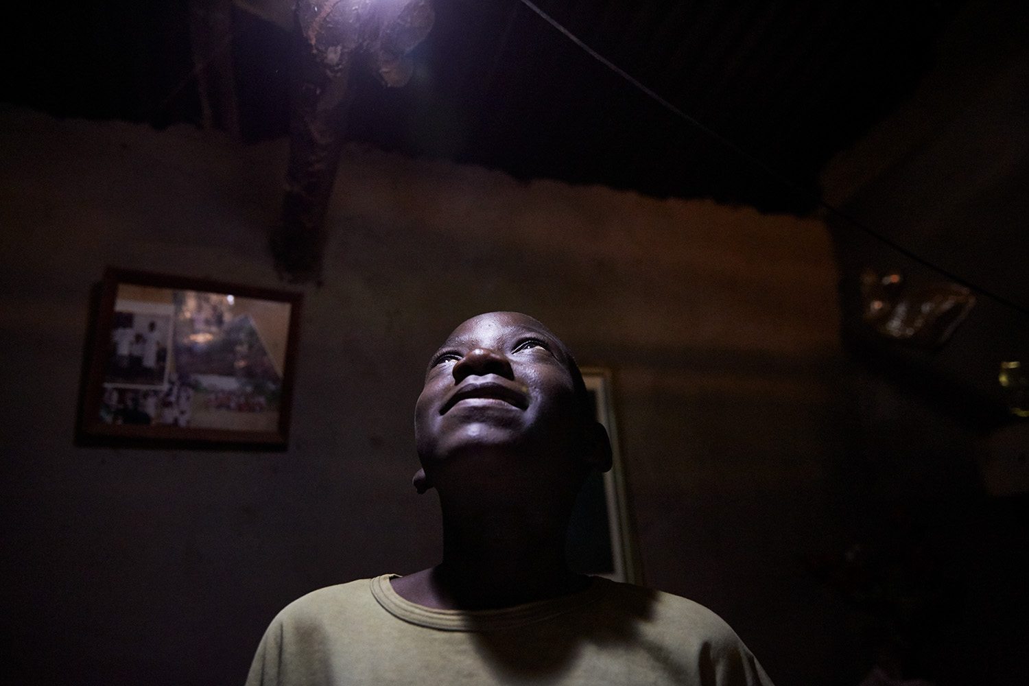  Jan Chumba (12) looks up at the solar battery run light at his home, Luchenza, Malawi, 2017. 