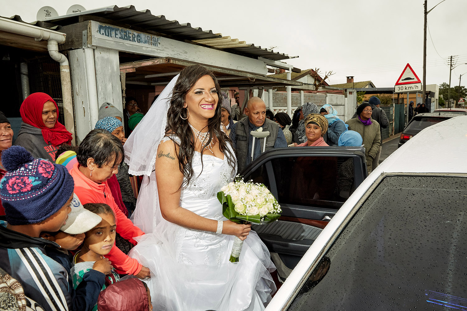  Surrounded by curious neighbours Chedino gets into the limousine which will take her to the wedding venue at Muizenberg Civic Centre, Heideveld, Cape Town, 2018. 