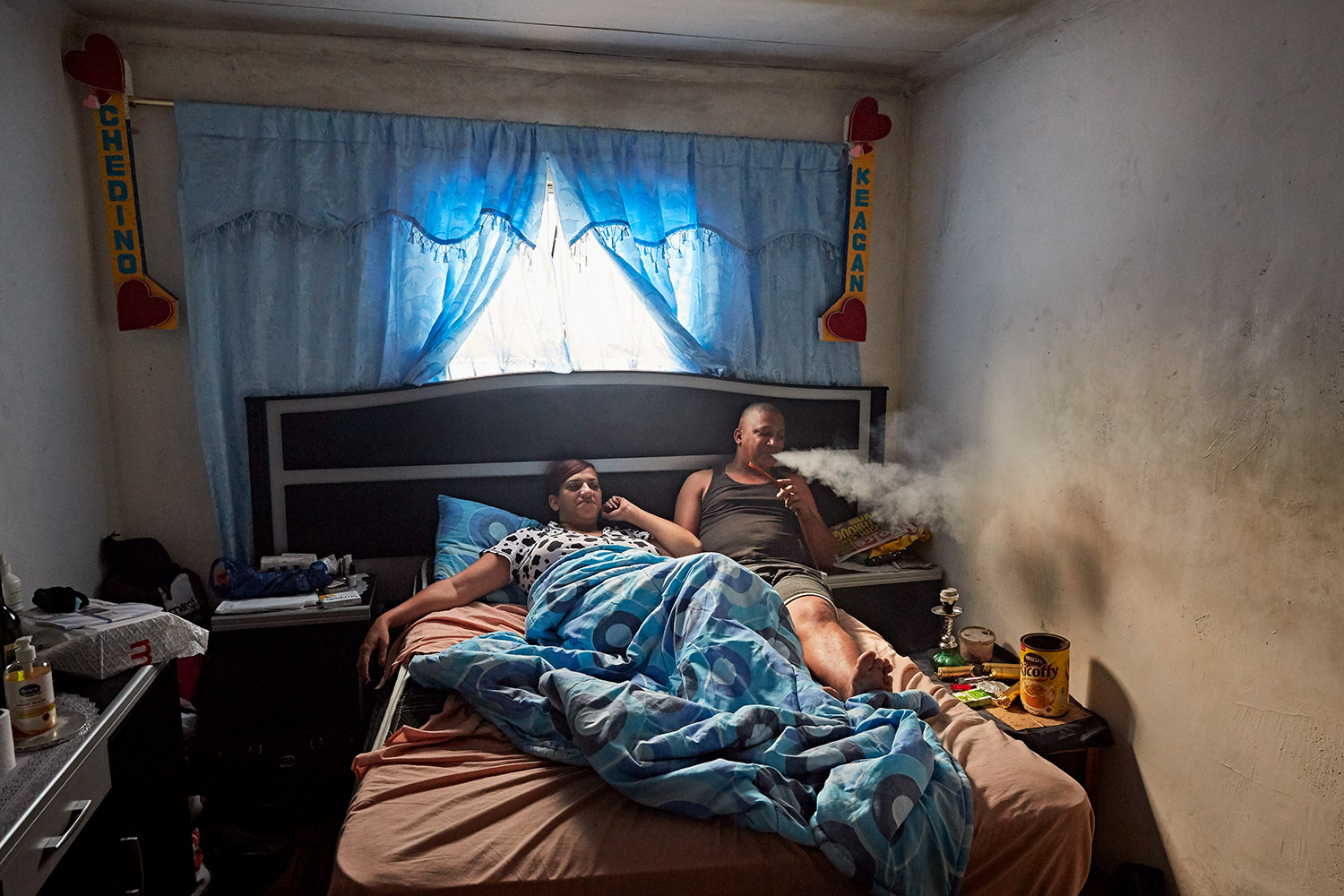  Chedino &amp; Keagan relax in bed on their one year anniversary, Hanover Park, Cape Town, 2019. 