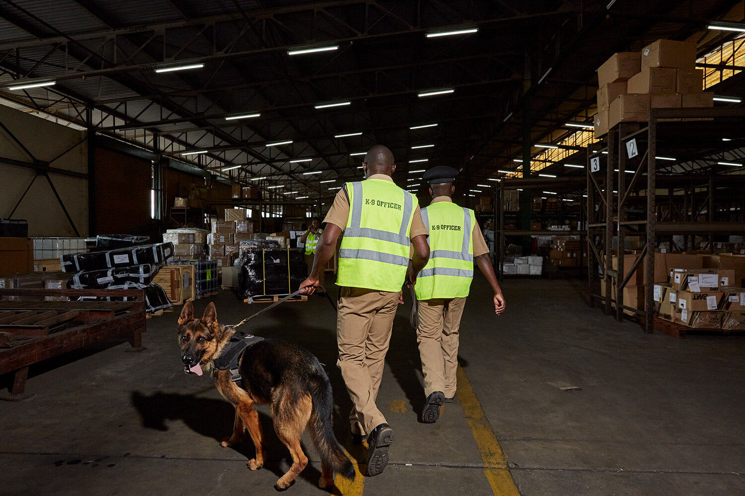  WDDU handlers Benjamin and Kinord, and dog Max walk through the imported cargo hall at Kamuzu International Airport (KIA), Lilongwe, Malawi, 2020. 