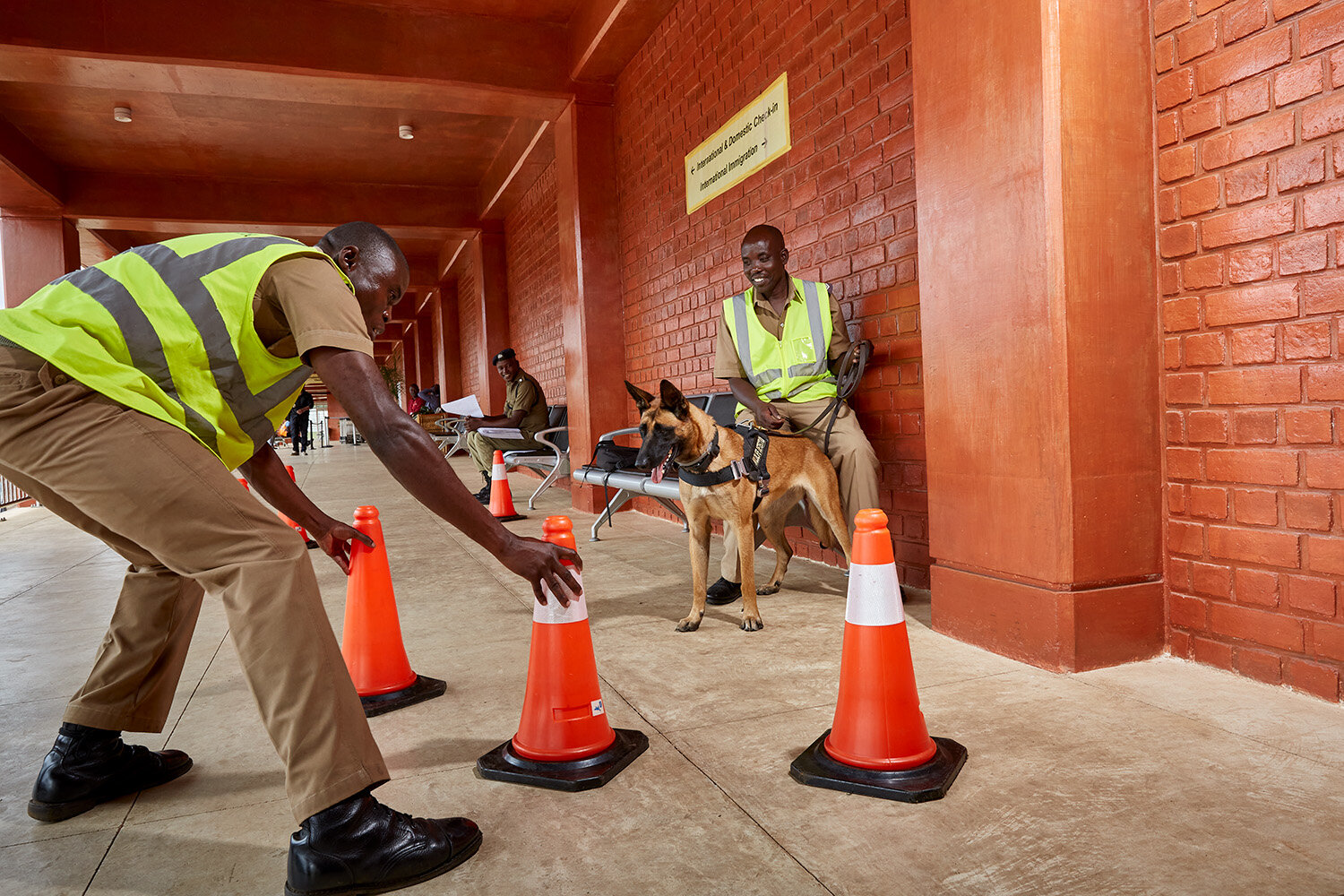  WDDU handlers Benjamin (left) and Kinord play with dog Danna while waiting to search departing passengers at Kamuzu International Airport (KIA), Lilongwe, Malawi, 2020. 